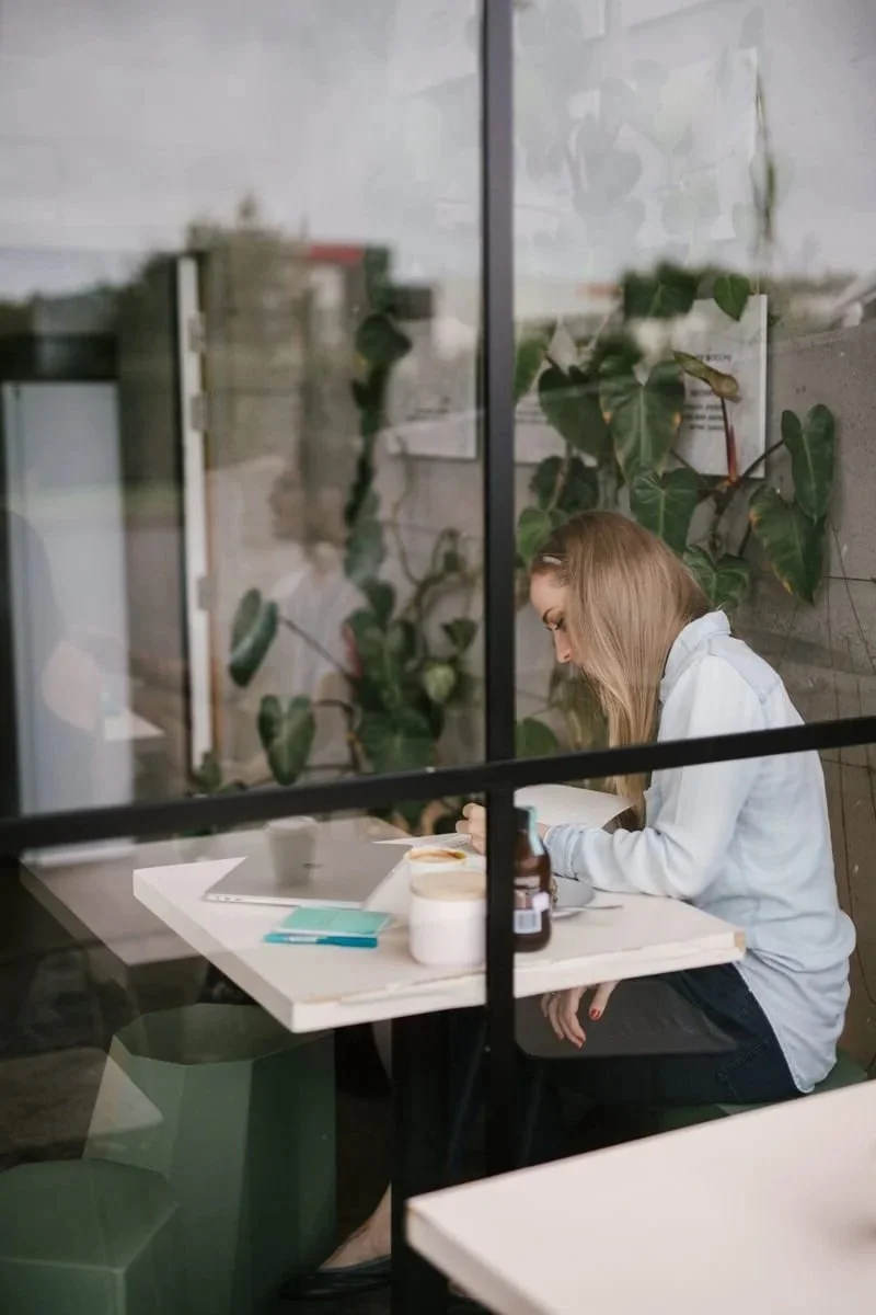 A website copywriter sits at a café table by a window, writing in a notebook delivering website copywriting services.
