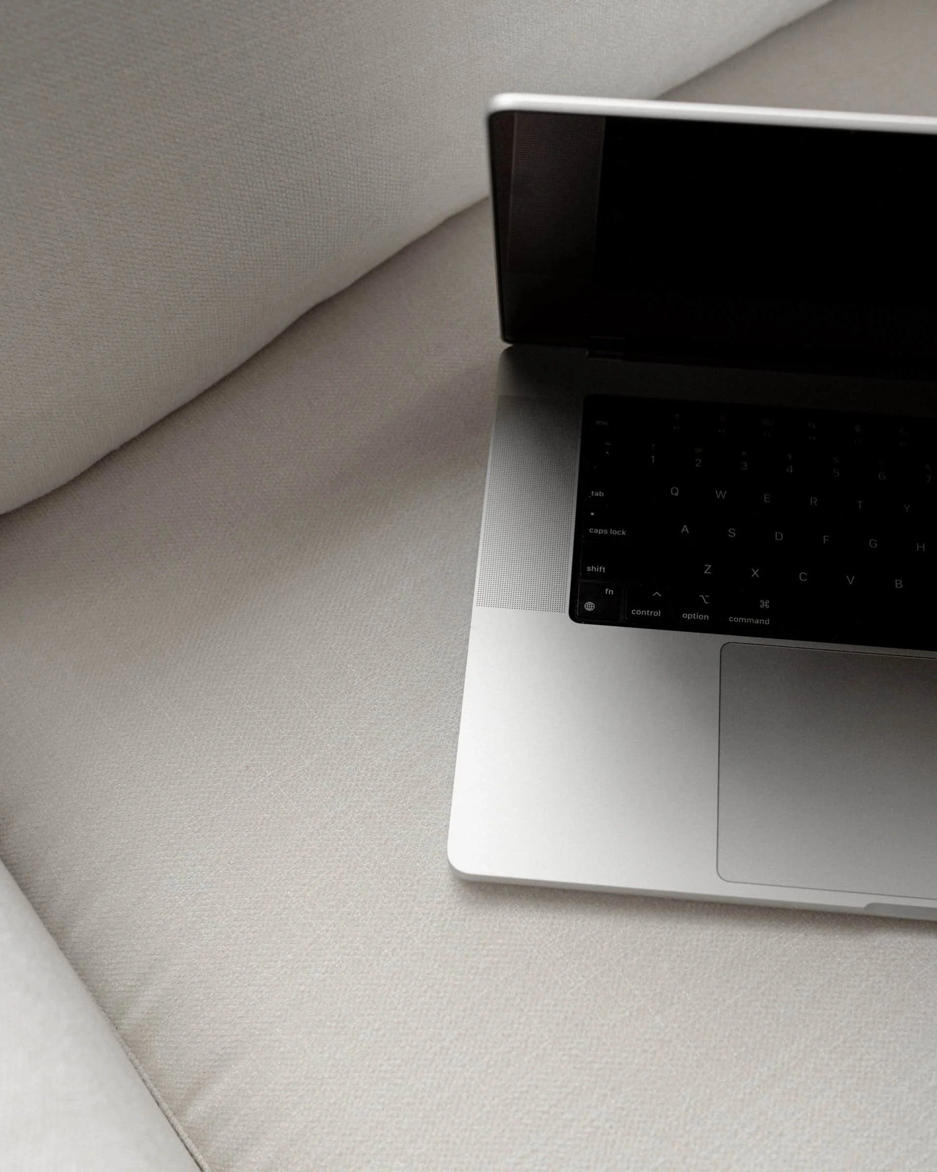 A partially open laptop sits on a light couch.