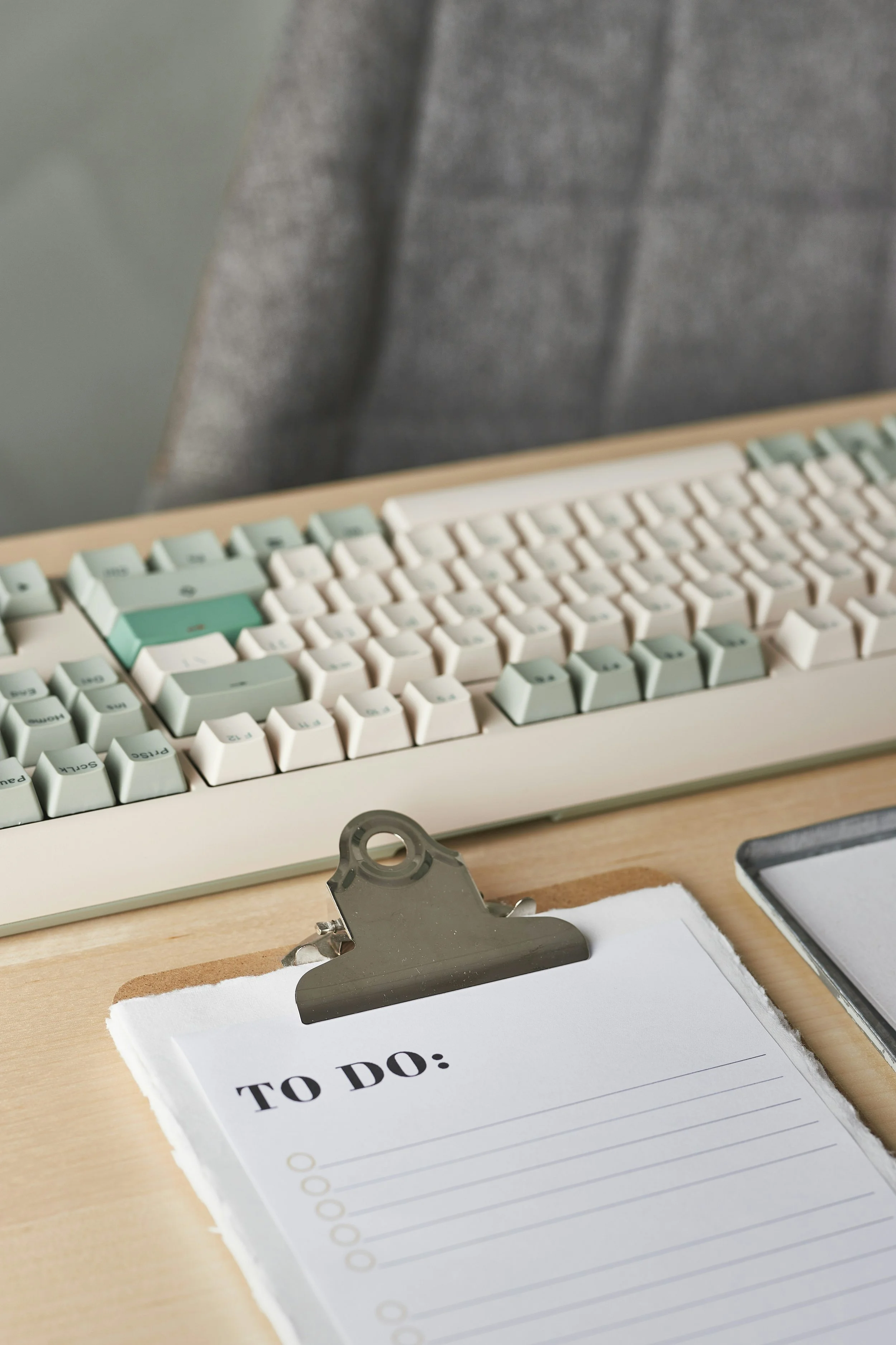 A white keyboard with blue keys and a to-do list on a light toned wooden desk