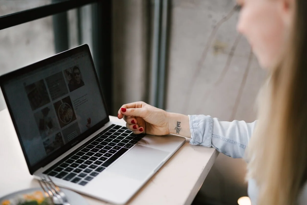 Website copywriter and website designer Yolie Stephenson working at laptop in cafe with a concrete wall and piping in the backgorund