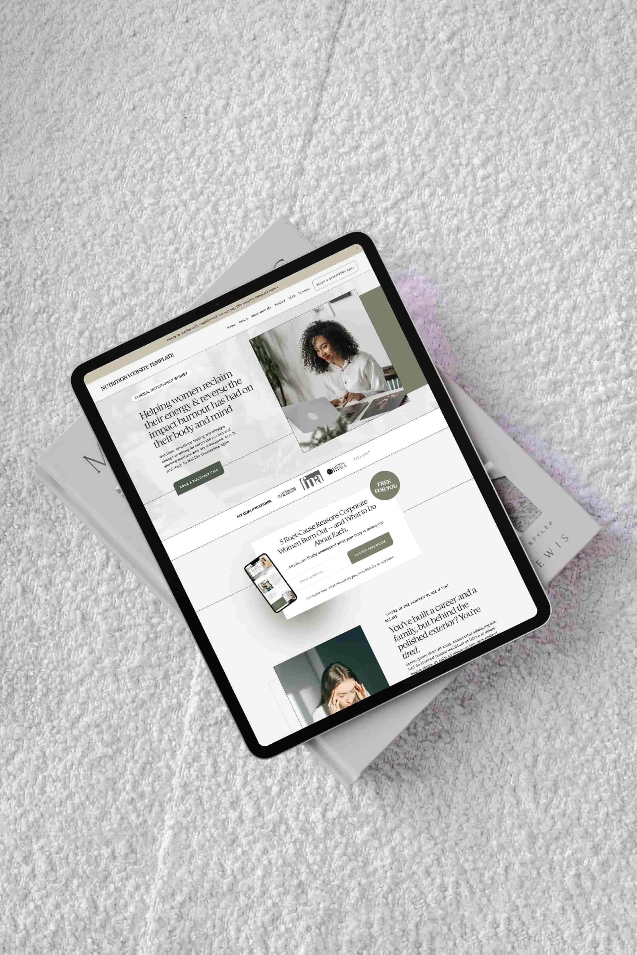 A tablet showing a wellness website designer’s work rests atop magazines on a textured, light-colored surface.