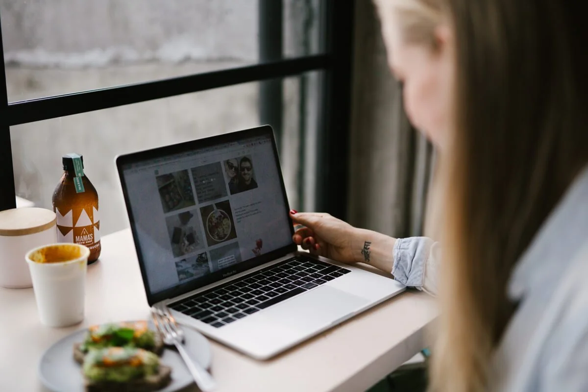 A health and wellness website designer works on her laptop by the window, coffee and avocado toast beside her for energy and inspiration.