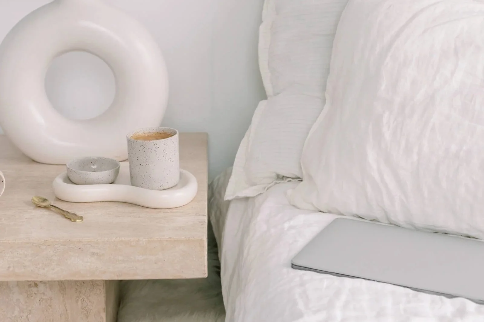Laptop used for wellness copywriting services on a bed ready to be picked up, with a coffee on the table nearby