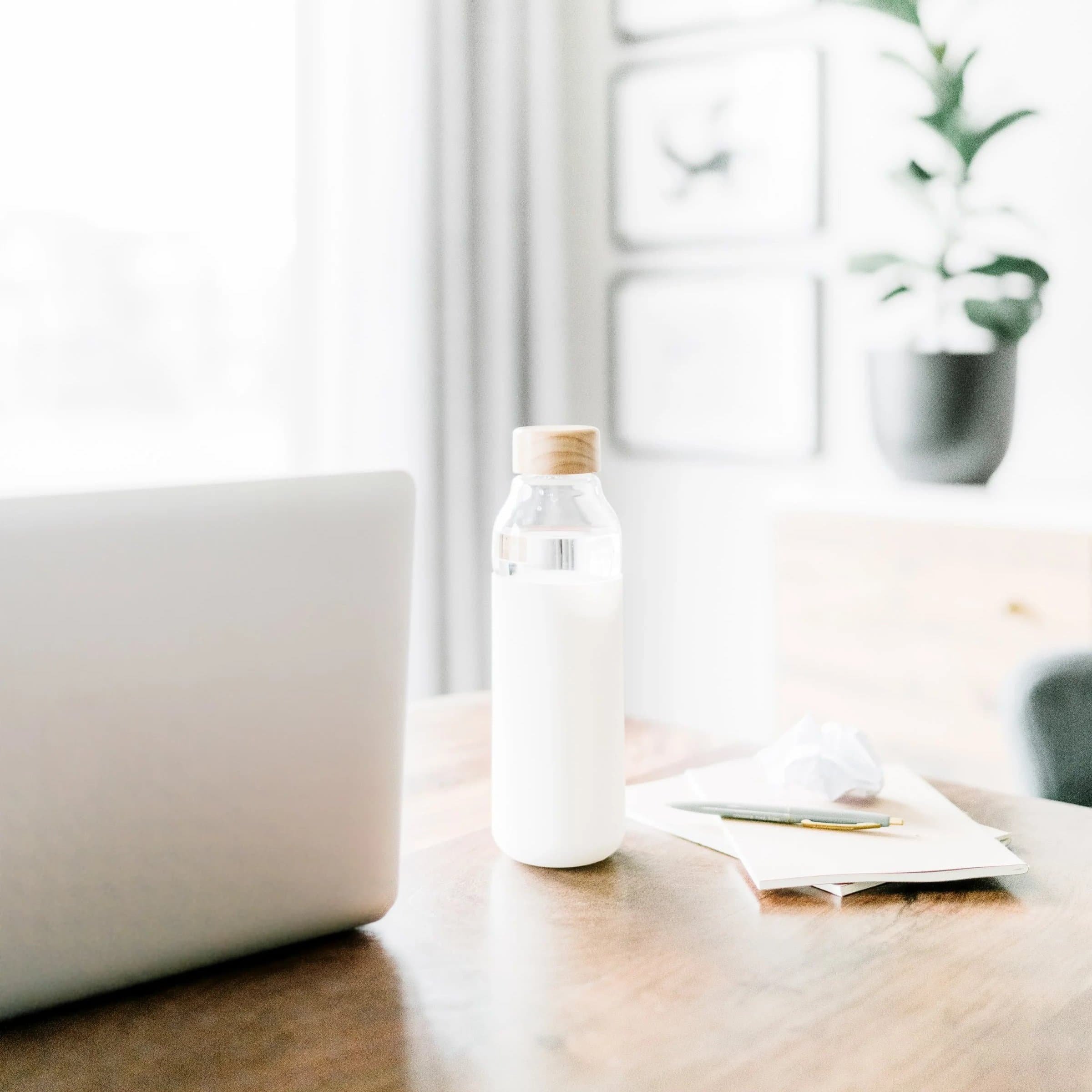 A bottle of water sits by a laptop and papers, perfect for a professional nutritionist in this bright, inviting workspace.