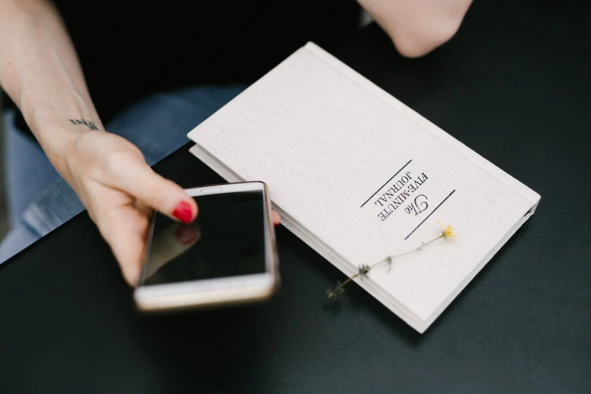 A Health and Wellness Copywriter texts a client with a Gratitude Journal nearby