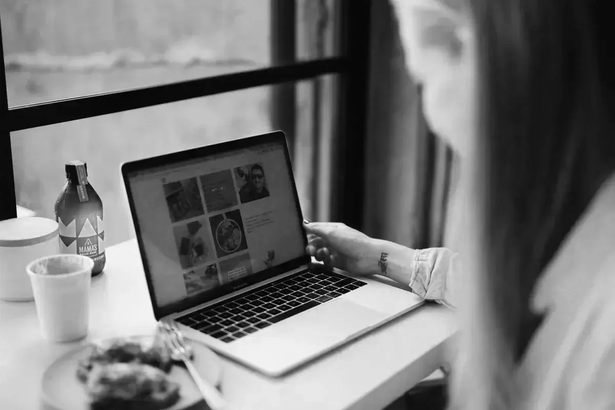 Health and wellness website designer working at desk with laptop open and healthy food images on it, with avocado toast, kombucha and tumeric latte by the side of the computer