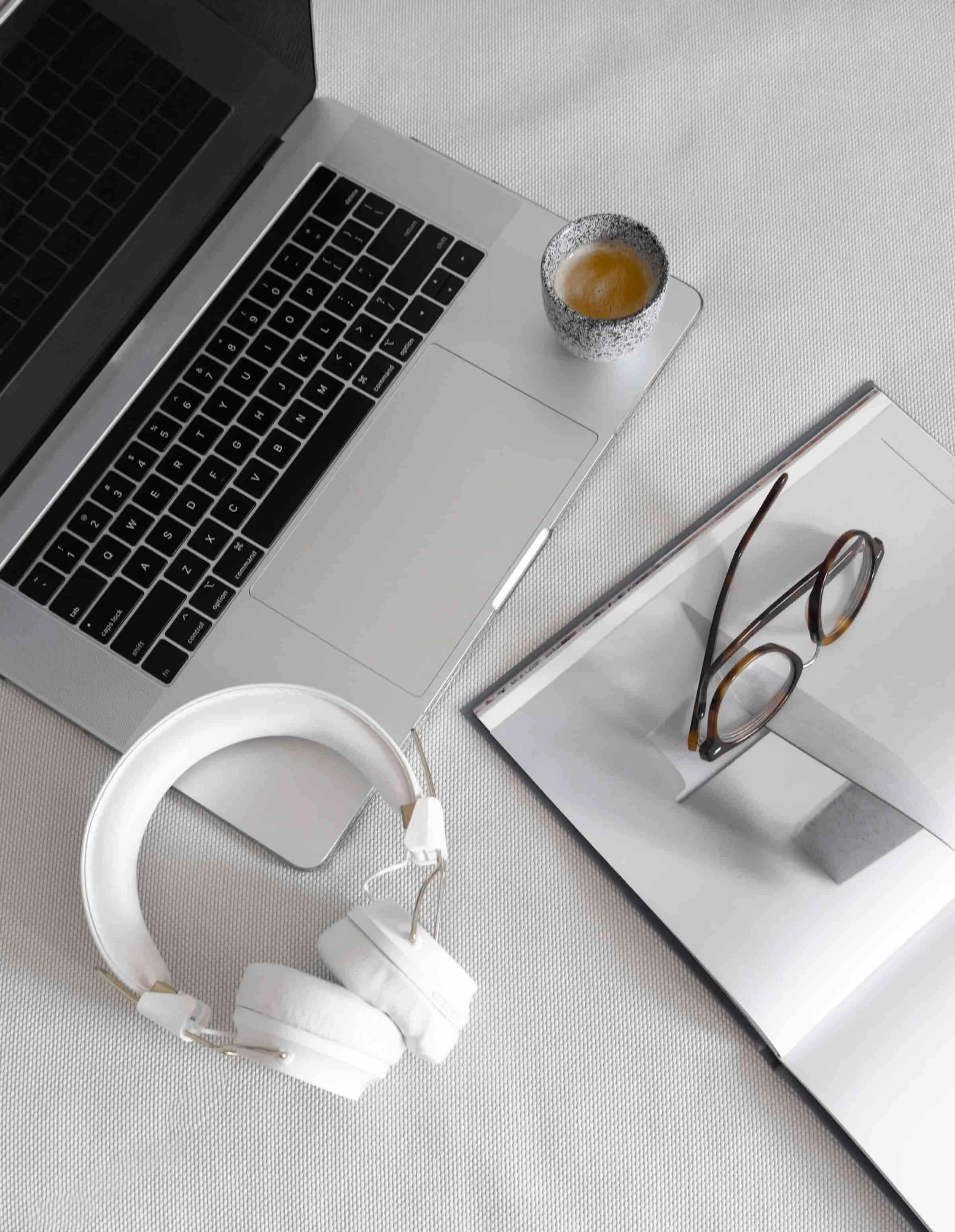 A laptop, headphones, coffee cup, eyeglasses, and an open magazine hint at wellness copywriting services in action.