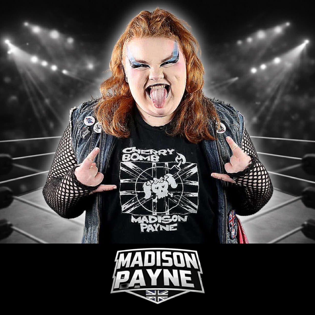 A woman with red hair, blue eye makeup, and a punk style is making a rock gesture with both hands in a wrestling ring. She is wearing a black t-shirt with a logo that says "Cherry Bomb" and "Madison Payne" and a denim vest with pins, with a dramatic spotlighted background.