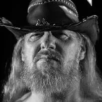 Close-up of a man with long hair and a beard wearing a cowboy hat.