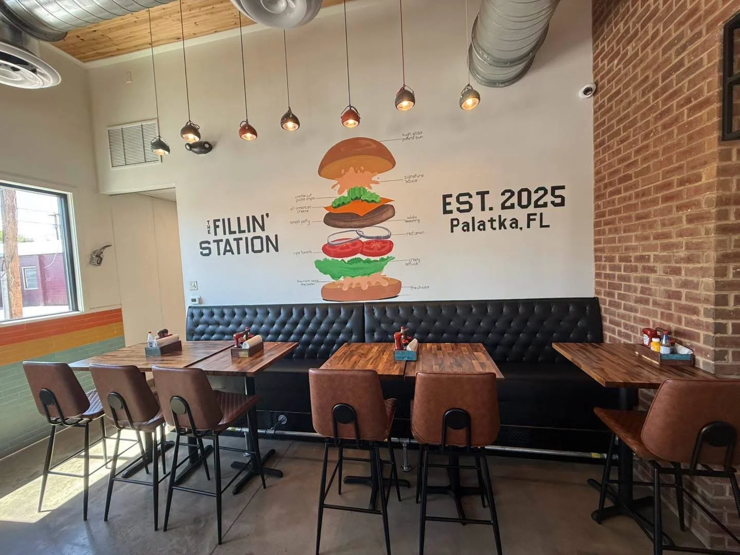 Interior dining room at The Fillin' Station featuring industrial decor, comfortable seating, and a custom burger mural.