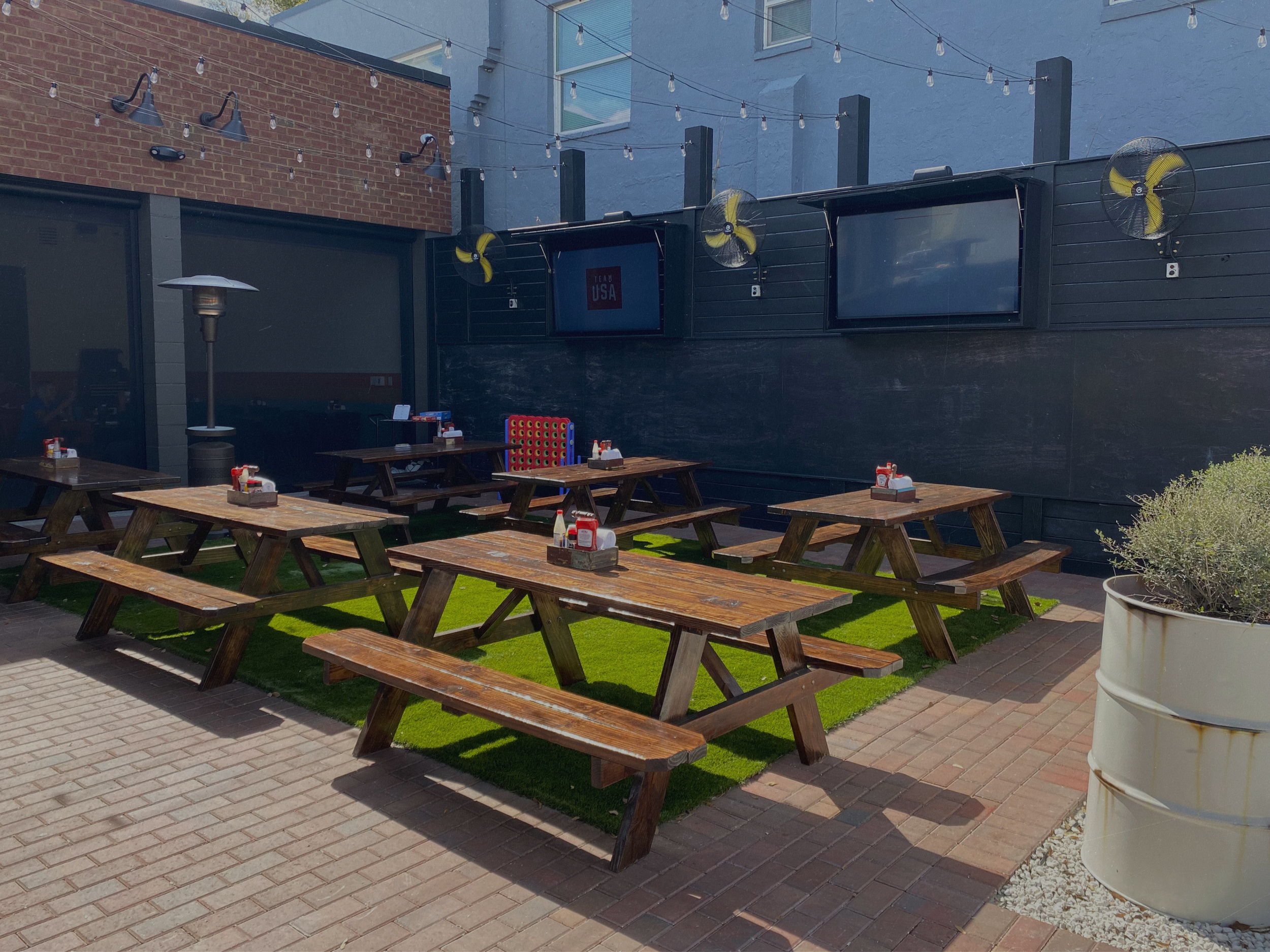 
Outdoor patio dining at The Fillin' Station with umbrellas, string lights, and guests enjoying a meal.