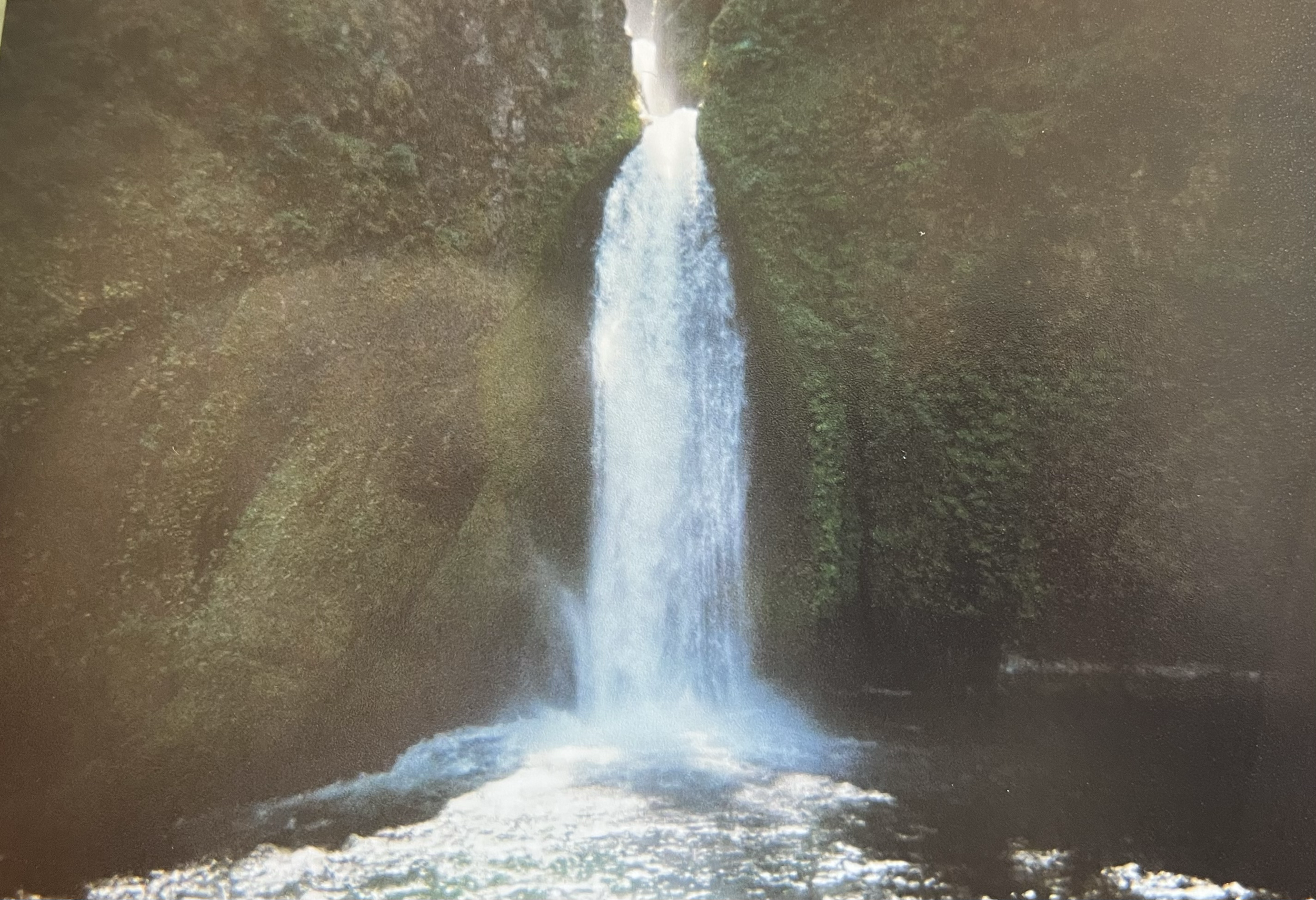 A tall waterfall cascading down from a rocky cliff surrounded by green trees.