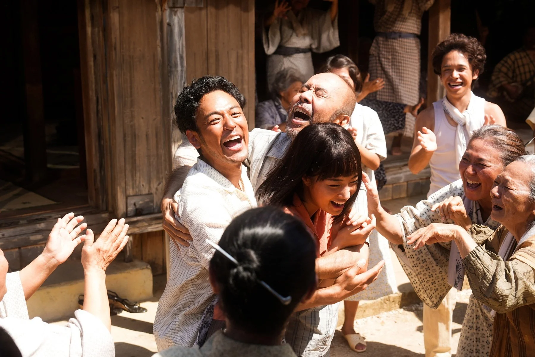 A group of people of different ages smiling and hugging each other outside on a sunny day, celebrating joyfully.