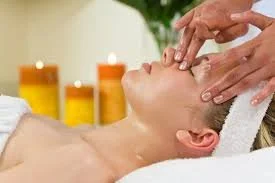 Person receiving a facial massage in a spa setting with candles in the background.