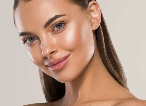 Close-up of a woman with clear skin, smiling slightly, with brown hair and blue eyes.