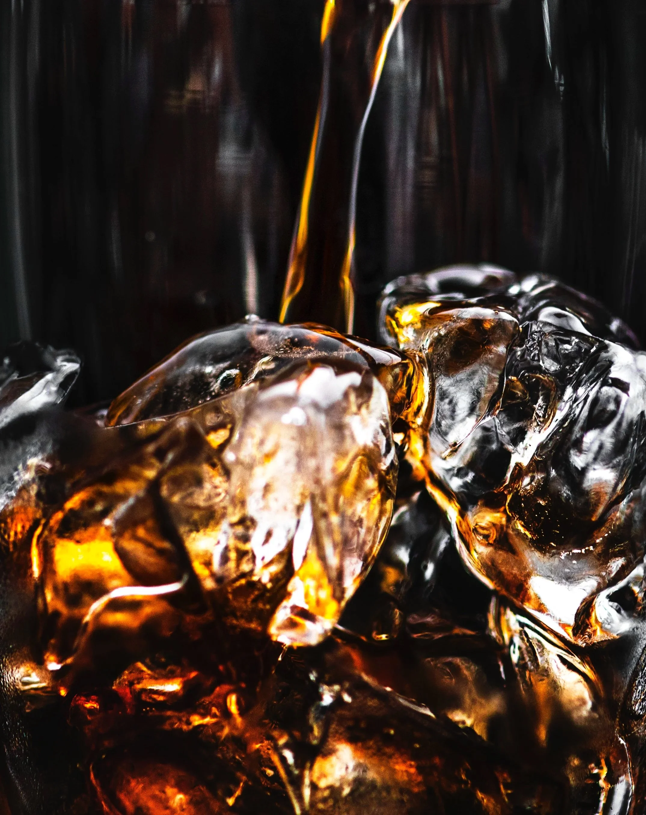 Close-up of ice cubes with dark cola being poured over them.