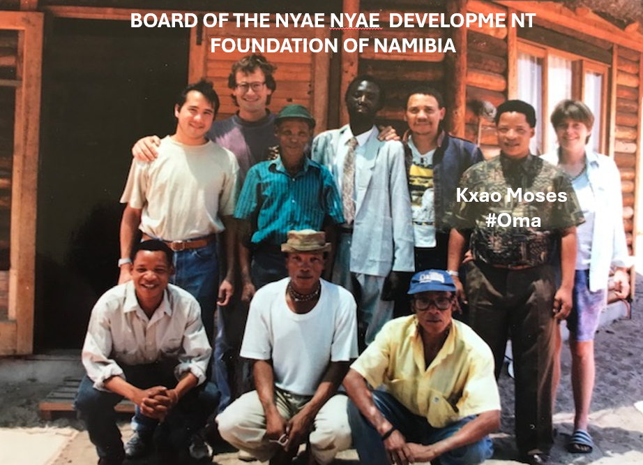 Group photograph of the Board of Directors of the Nyae Nyae Development Foundation in the early 1990s, taken at Baraka in the Nyae Nyae region of Namibia, showing board members outside a wooden building.