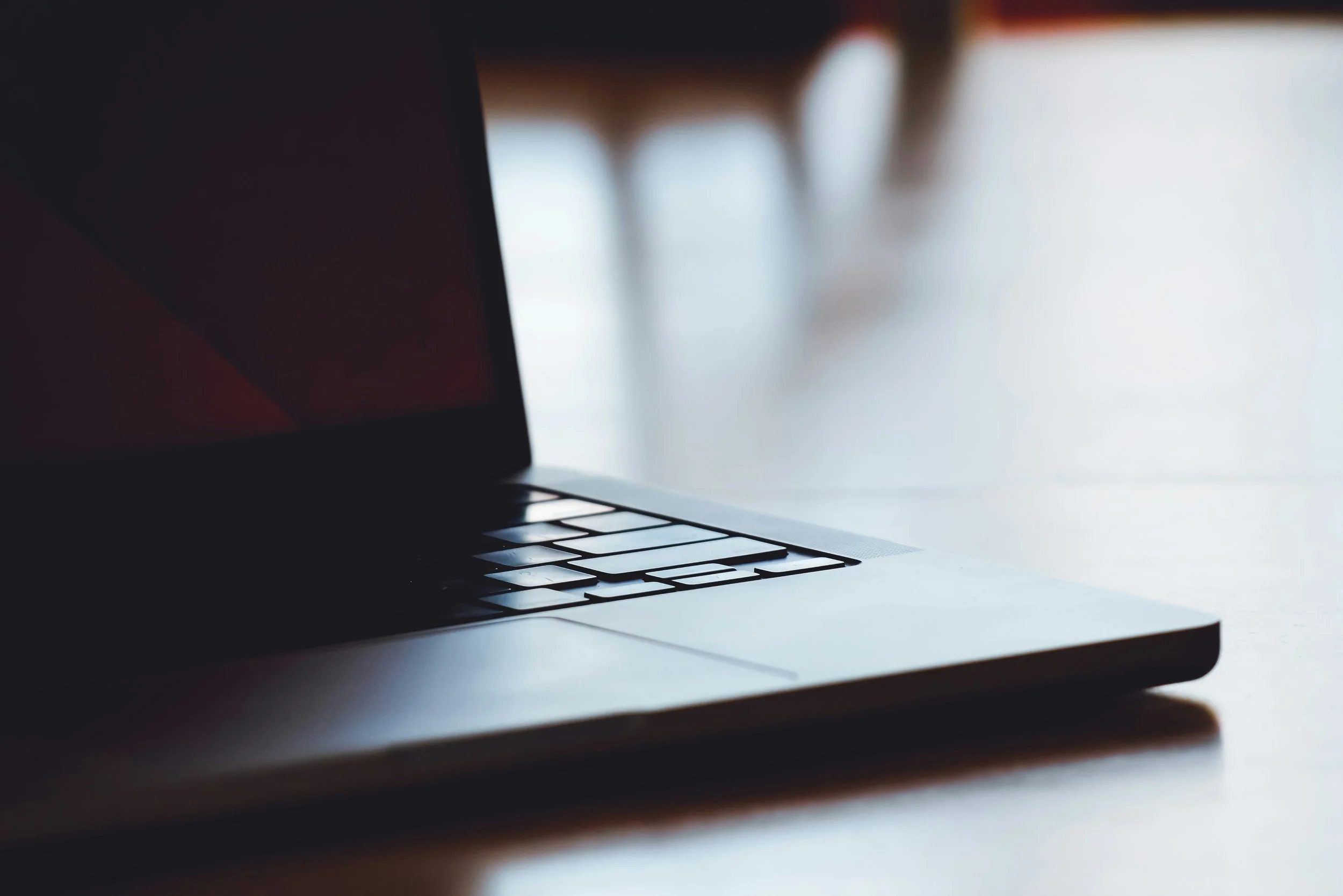 Close-up of a laptop on a wooden table with the screen turned off, background blurred.