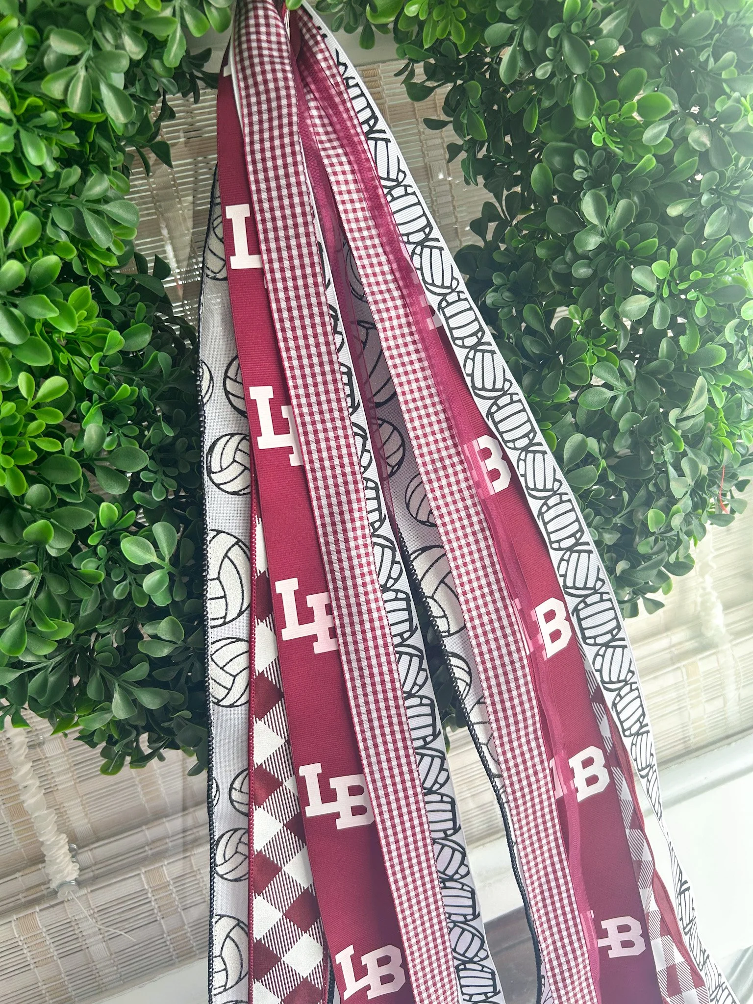 Multiple ribbons with sports and school related patterns hanging from a boxwood wreath.