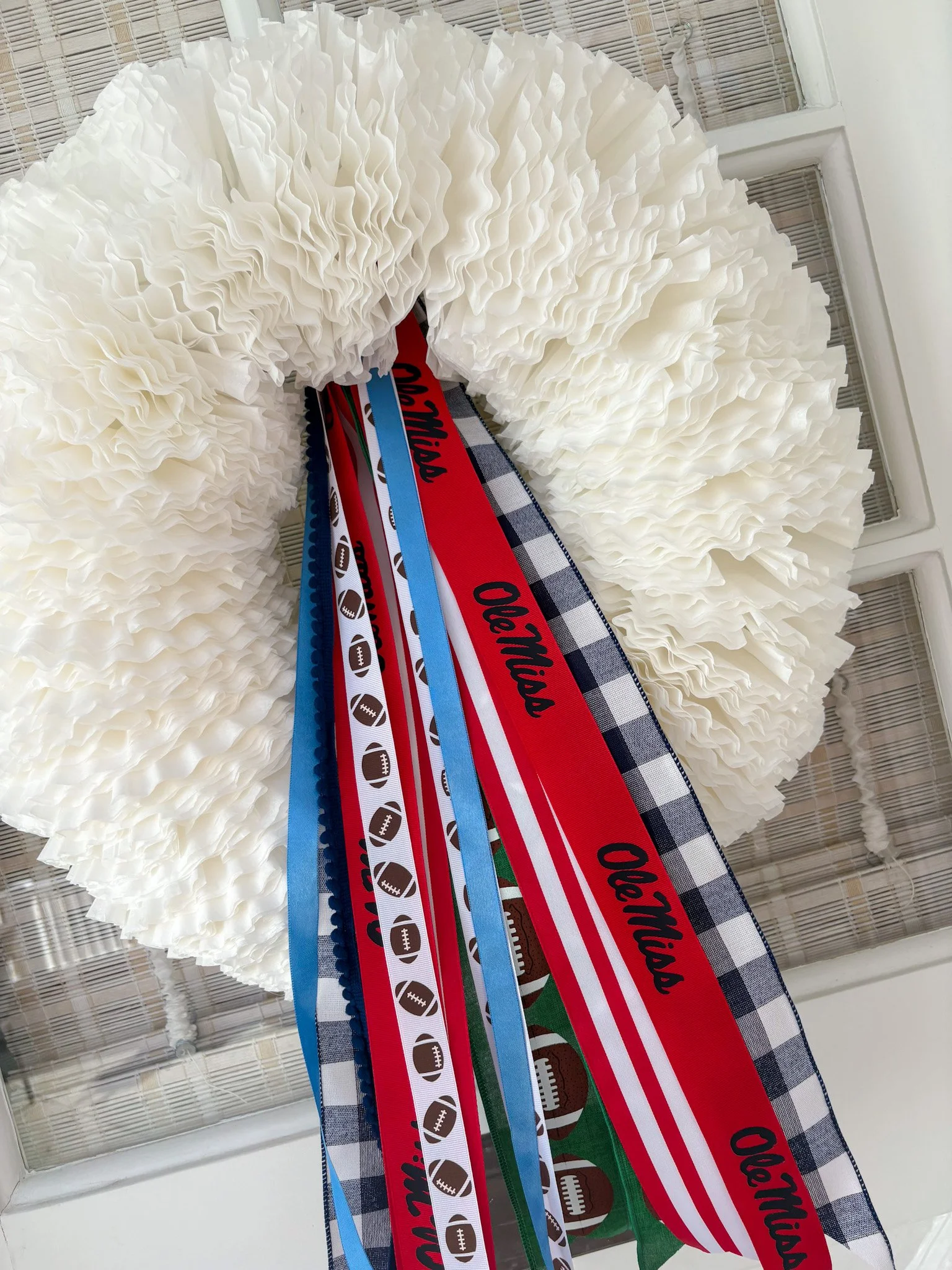 Large white pom-pom wreath with ribbons featuring football-themed patterns and Mississippi written on some ribbons.
