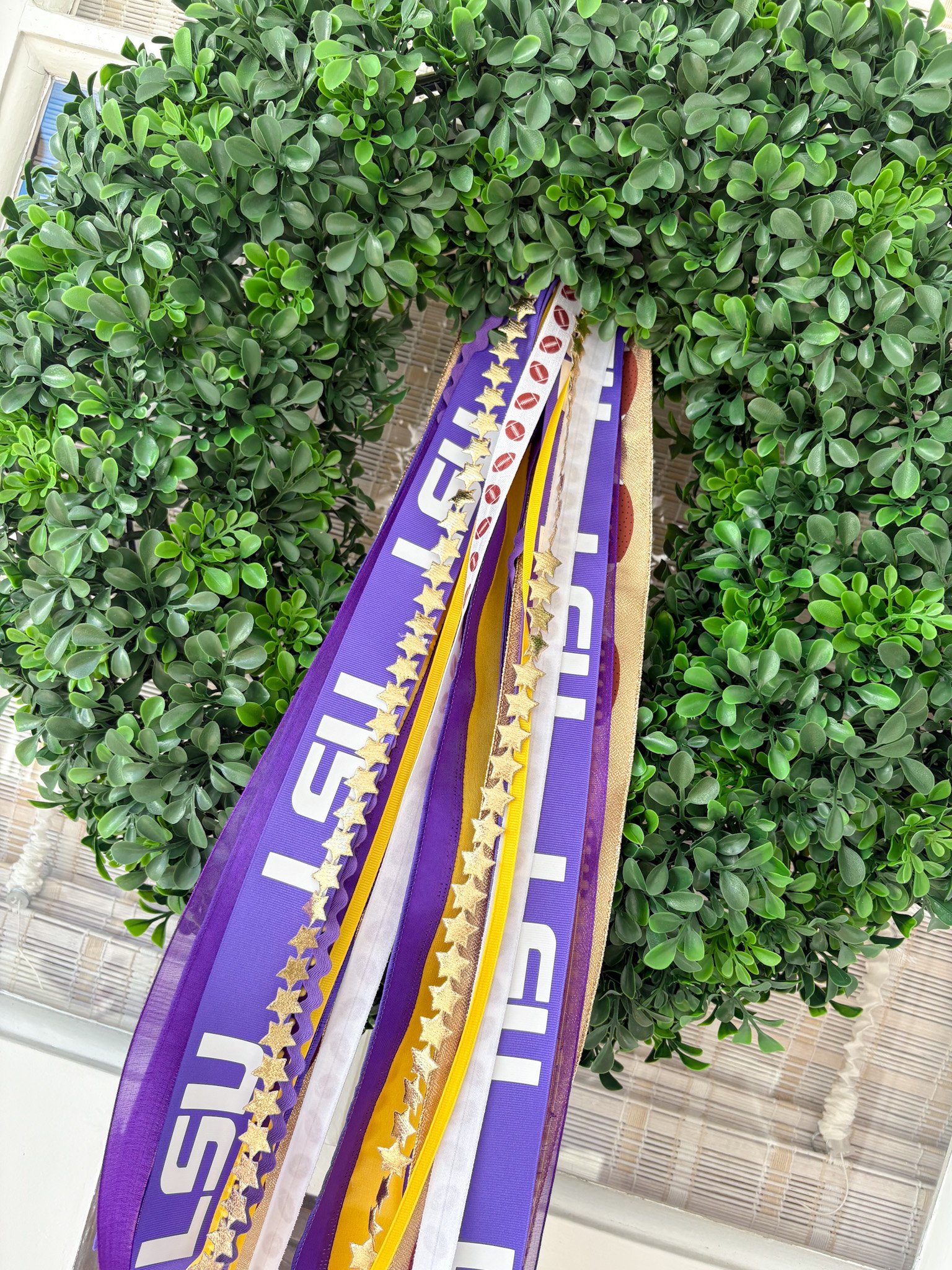 Colorful Louisiana ribbon wreath decorated with purple, white, yellow, and gold ribbons, hanging on a green wreath.