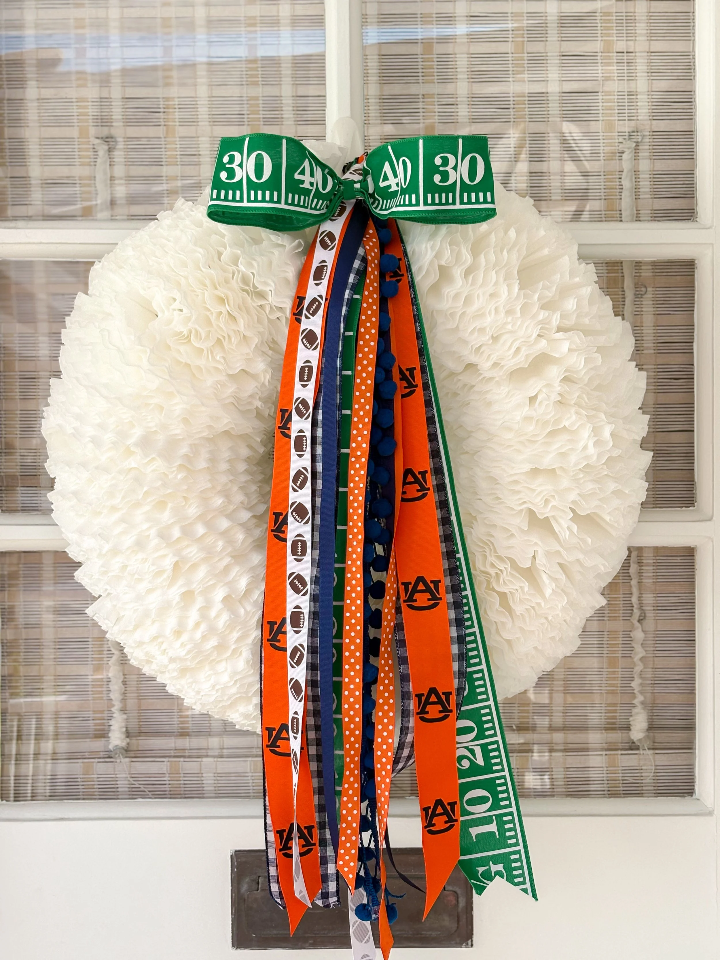 Football-themed wreath with orange, white, blue, and green ribbons, including University and football patterns, hanging on cottage door.