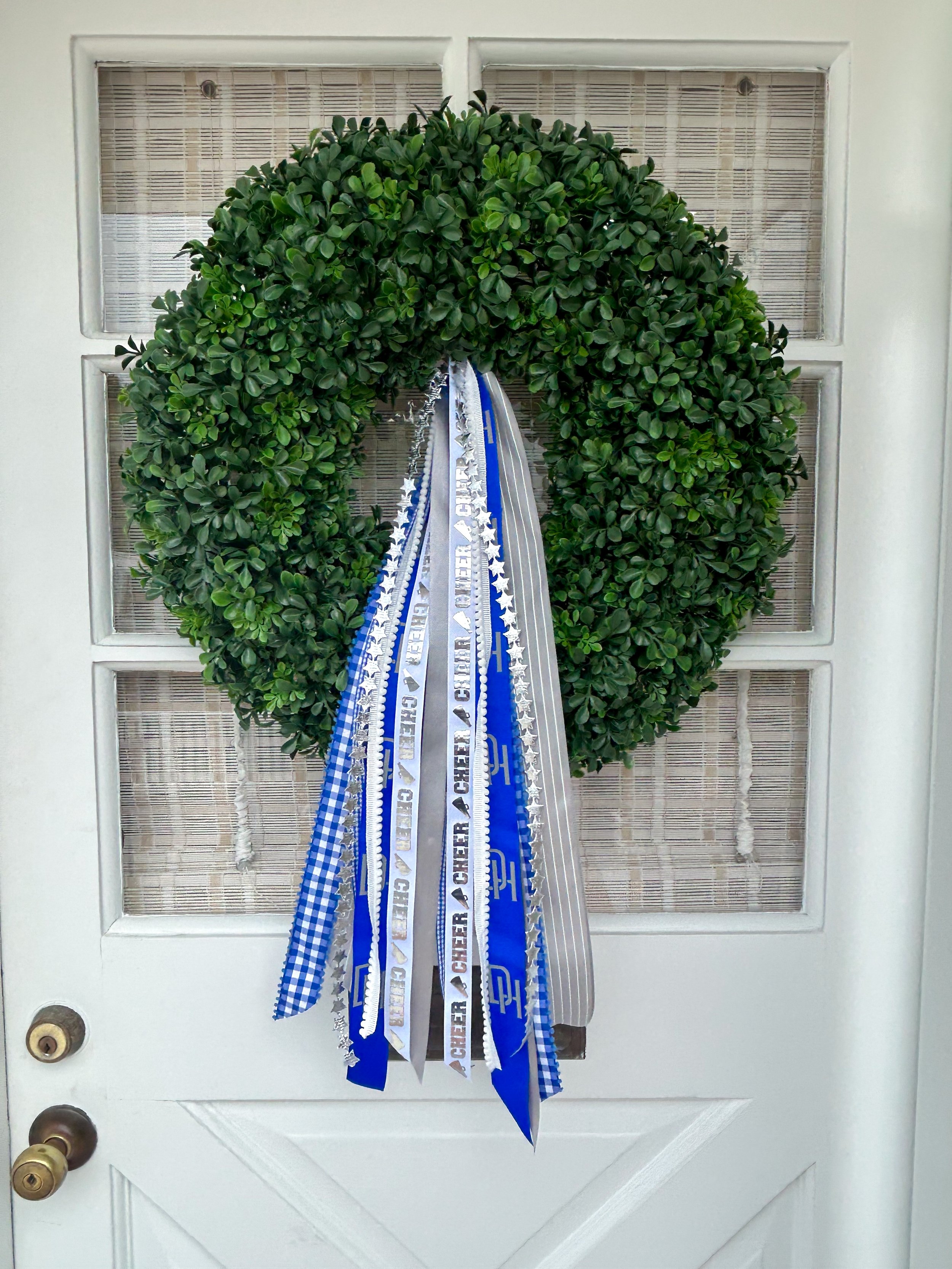 A green wreath with decorative ribbons hanging in front of a white door.