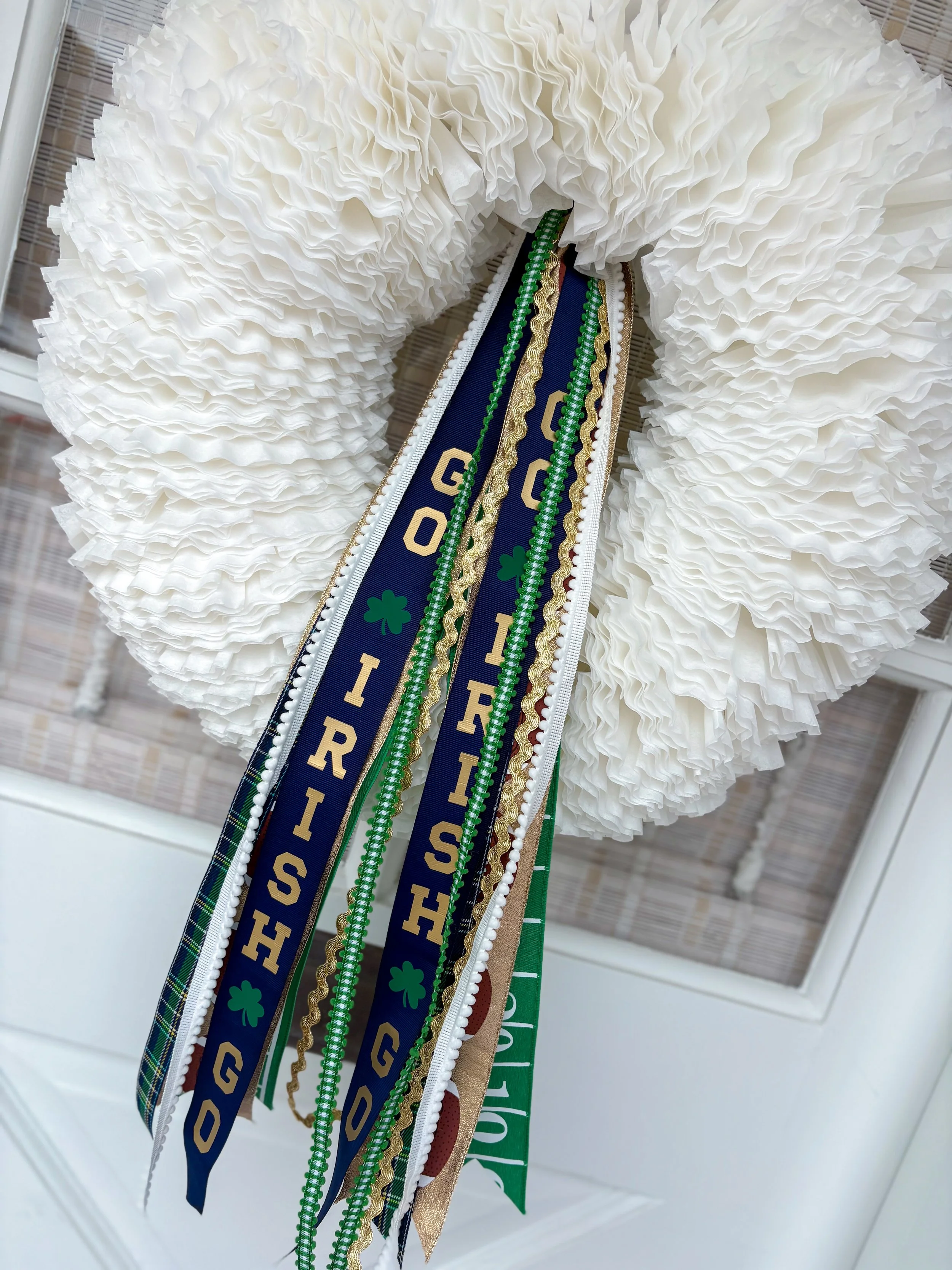 A game day wreath decorated with green ribbons, gold accents, and a blue ribbon that reads "Go Irish" with shamrock symbols.