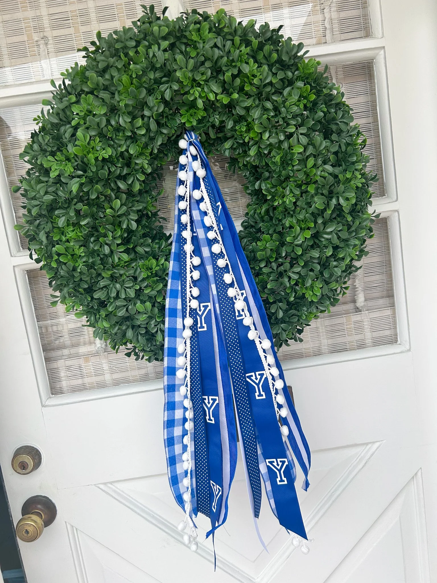 A green wreath decorated with blue and white ribbons hanging on a white door.