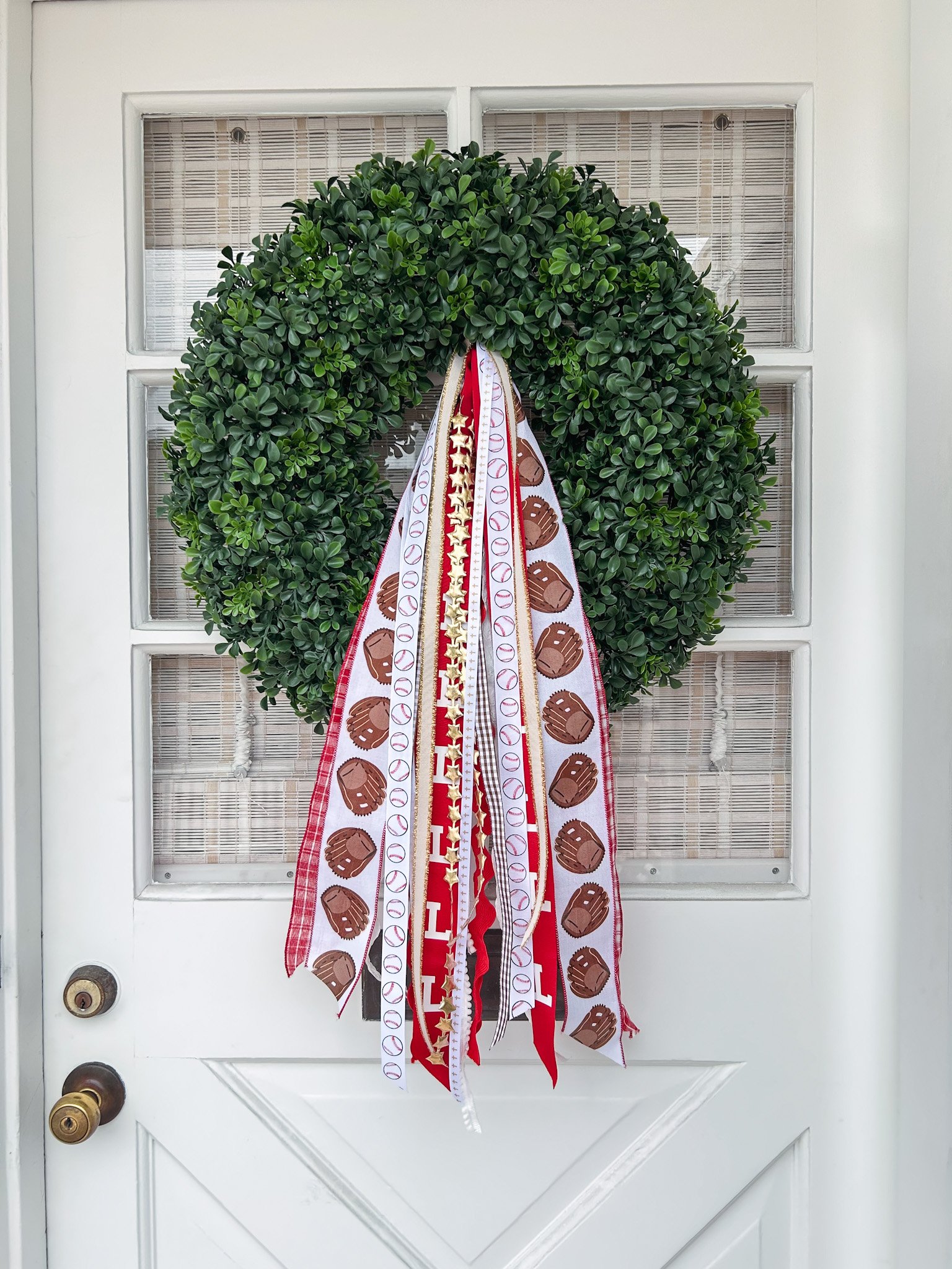 Green wreath decorated with ribbons and sports-themed ribbons hanging down, attached to a white door with glass panels.