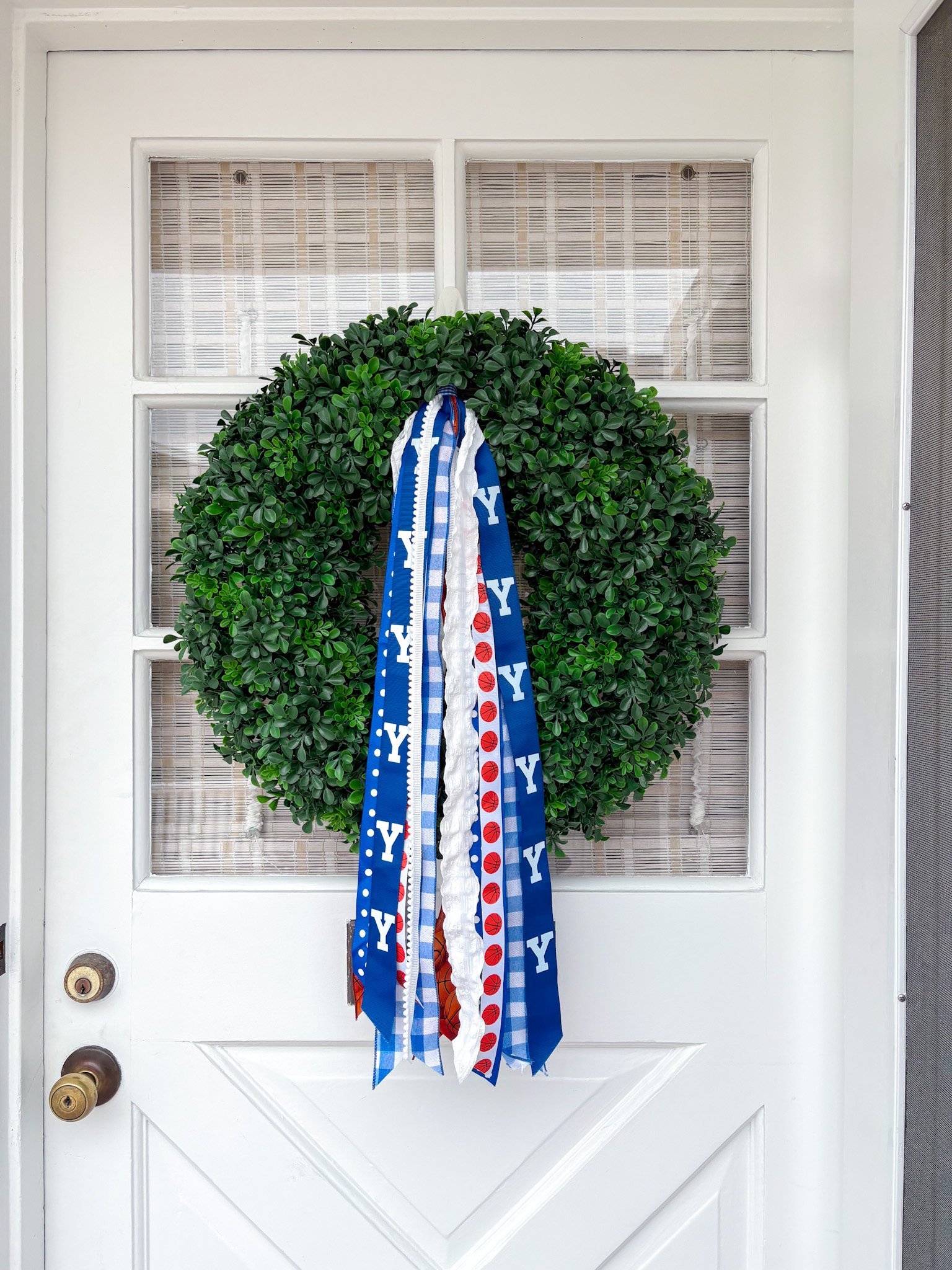 Green door with a large green wreath hanging on it, decorated with blue and white ribbons, and a red and white baseball-themed ribbon at the center.