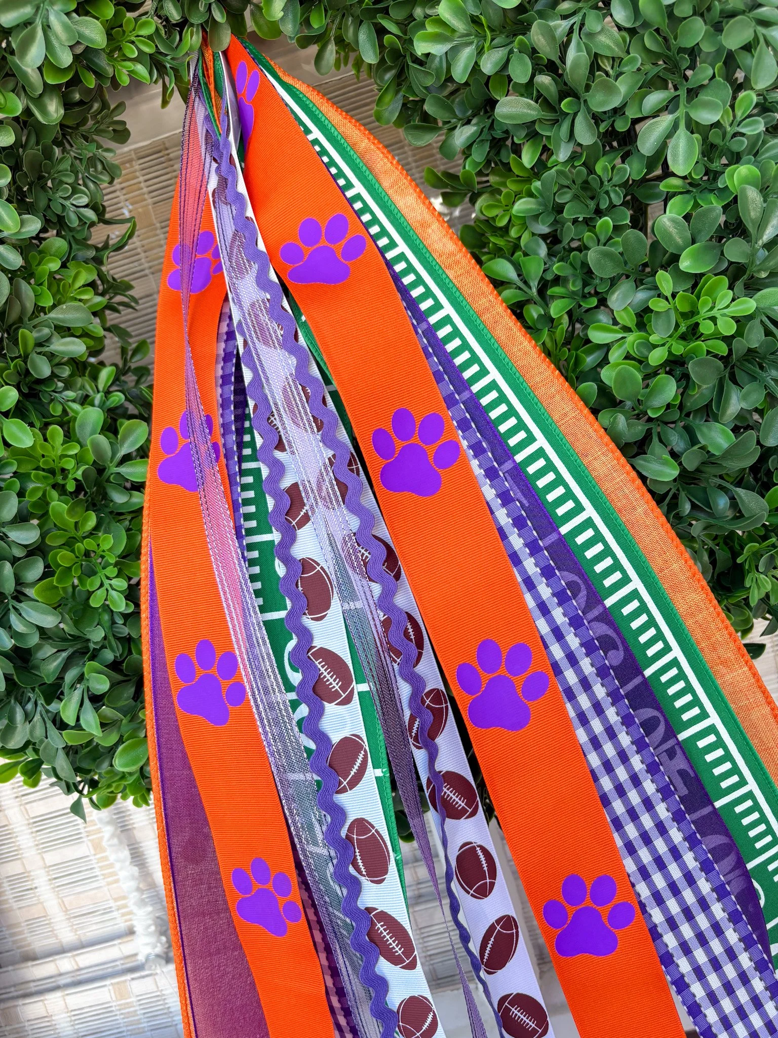 Decorative ribbons featuring football and paw print patterns hanging on a green leafy background.