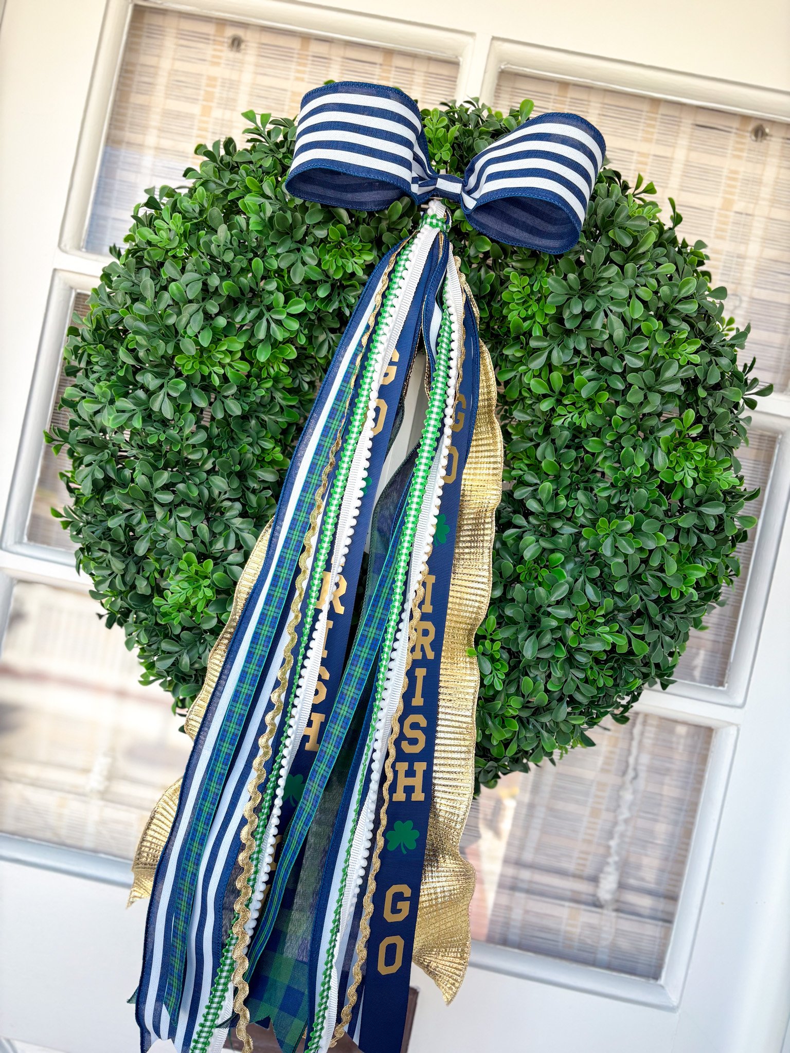 A decorative green wreath with a blue, white, and gold ribbon bow and various ribbons hanging down, displayed on a door.