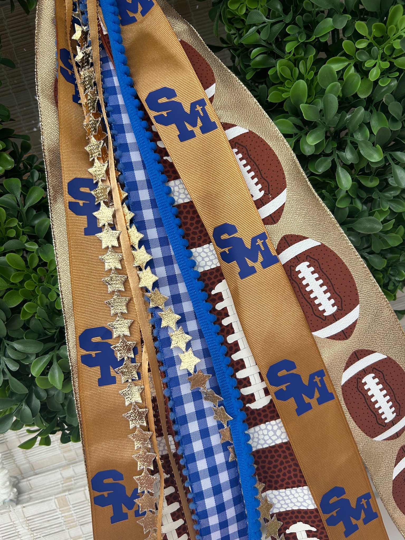 Multiple ribbons with Santa Margarita logo, gold and blue stars, and football-themed patterns, placed on green wreath.