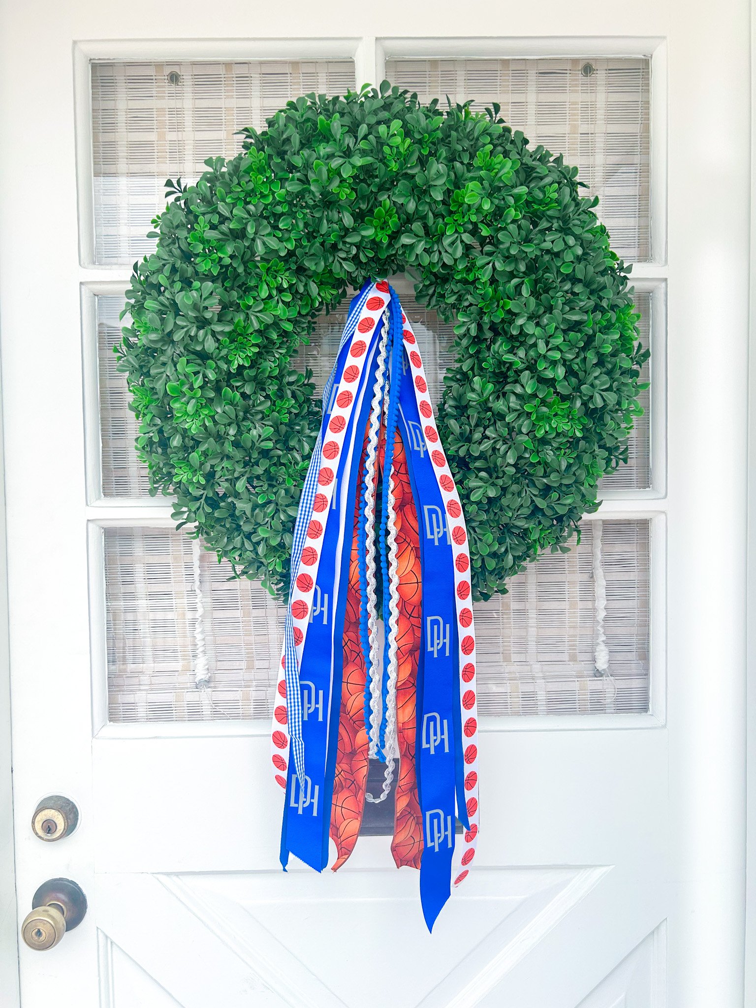 A decorative wreath with ribbons hanging on a front door, featuring basketballs.
