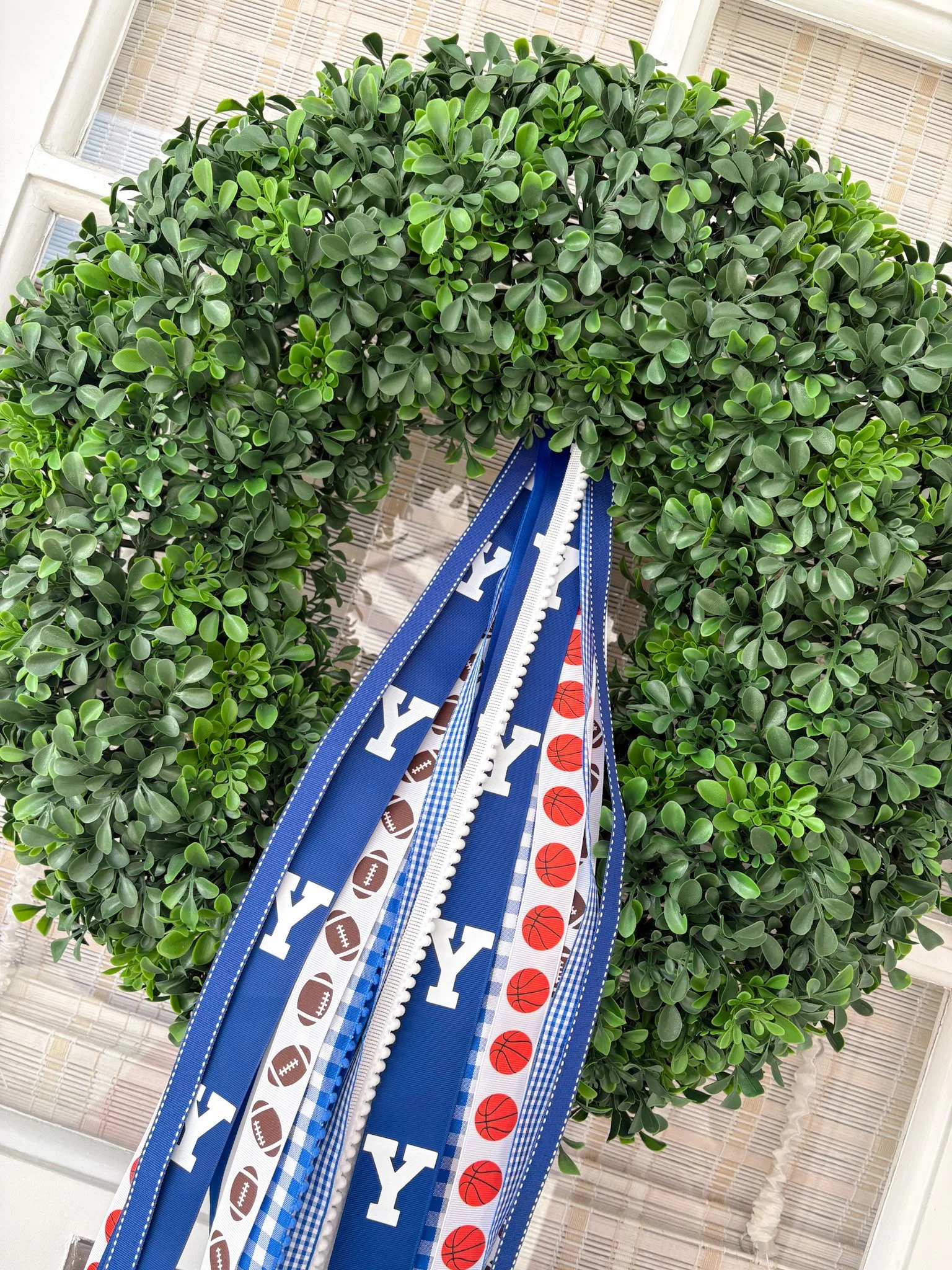 A circular green wreath with university and sports ribbons hanging in the center, featuring the letter "Y" and sports balls.