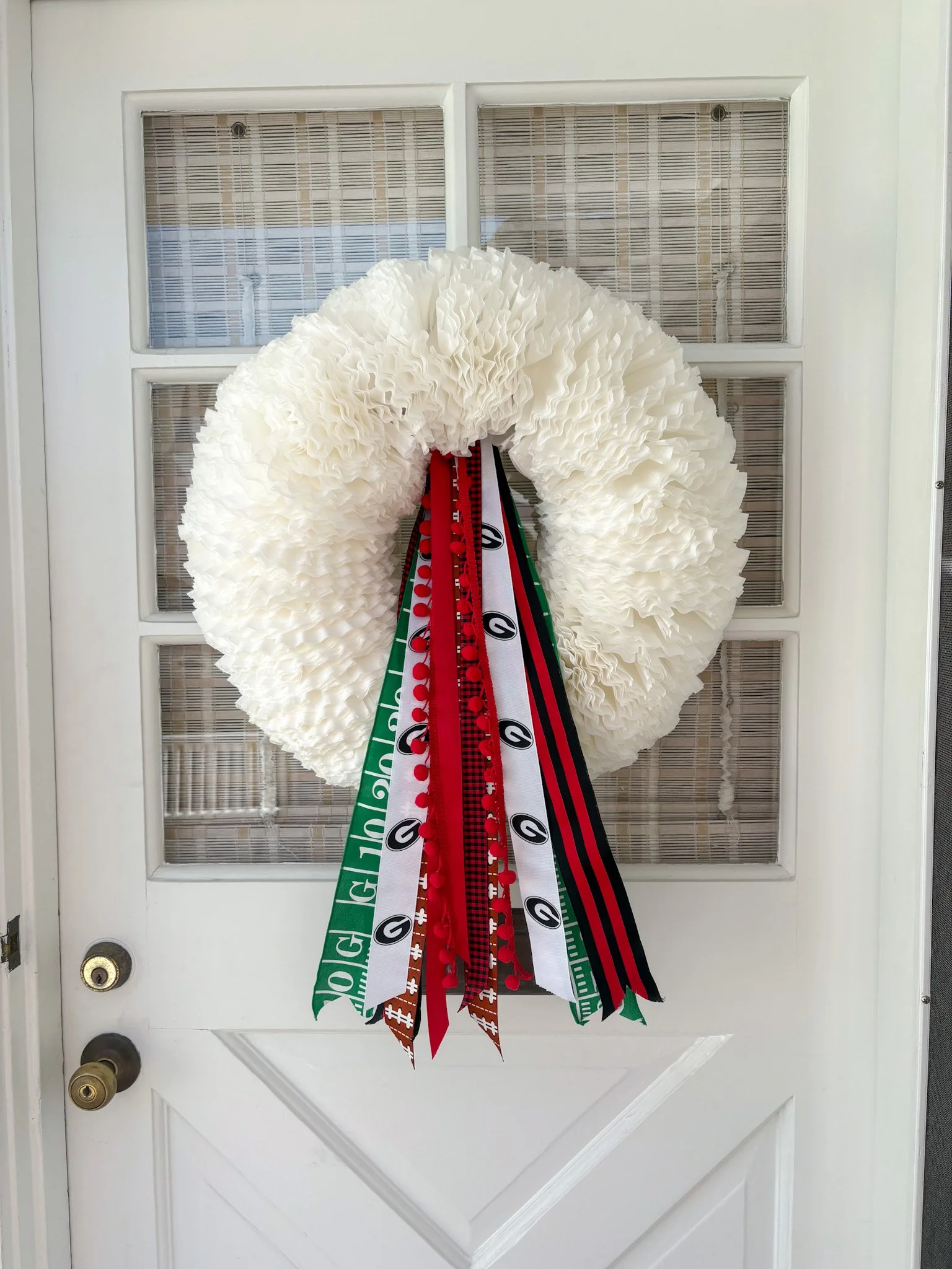 White wreath with multiple red ribbons hanging down, attached to a door.