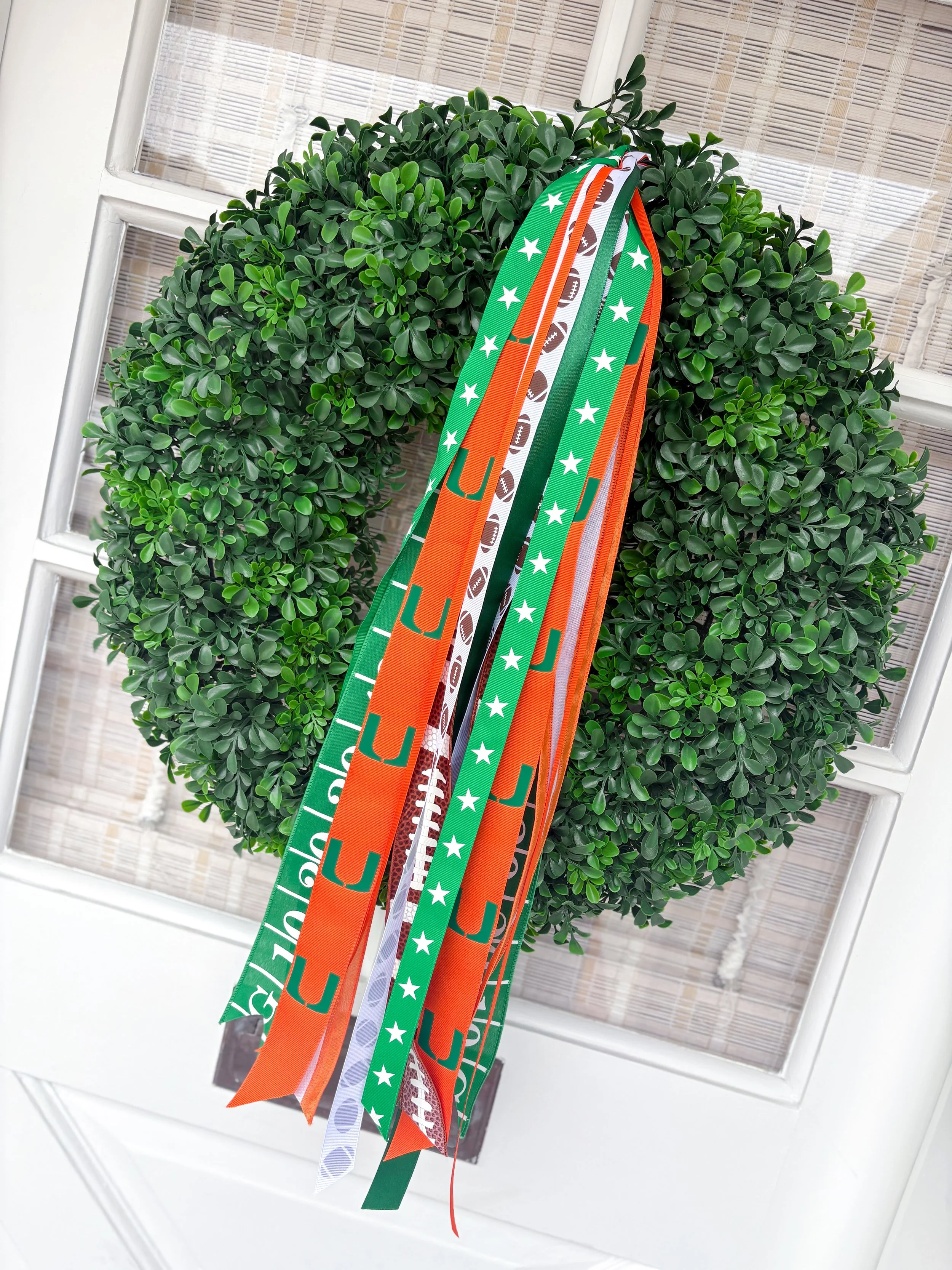 Green decorative wreath with hanging ribbons in orange, green, white, and brown with football and Hurricane themes.