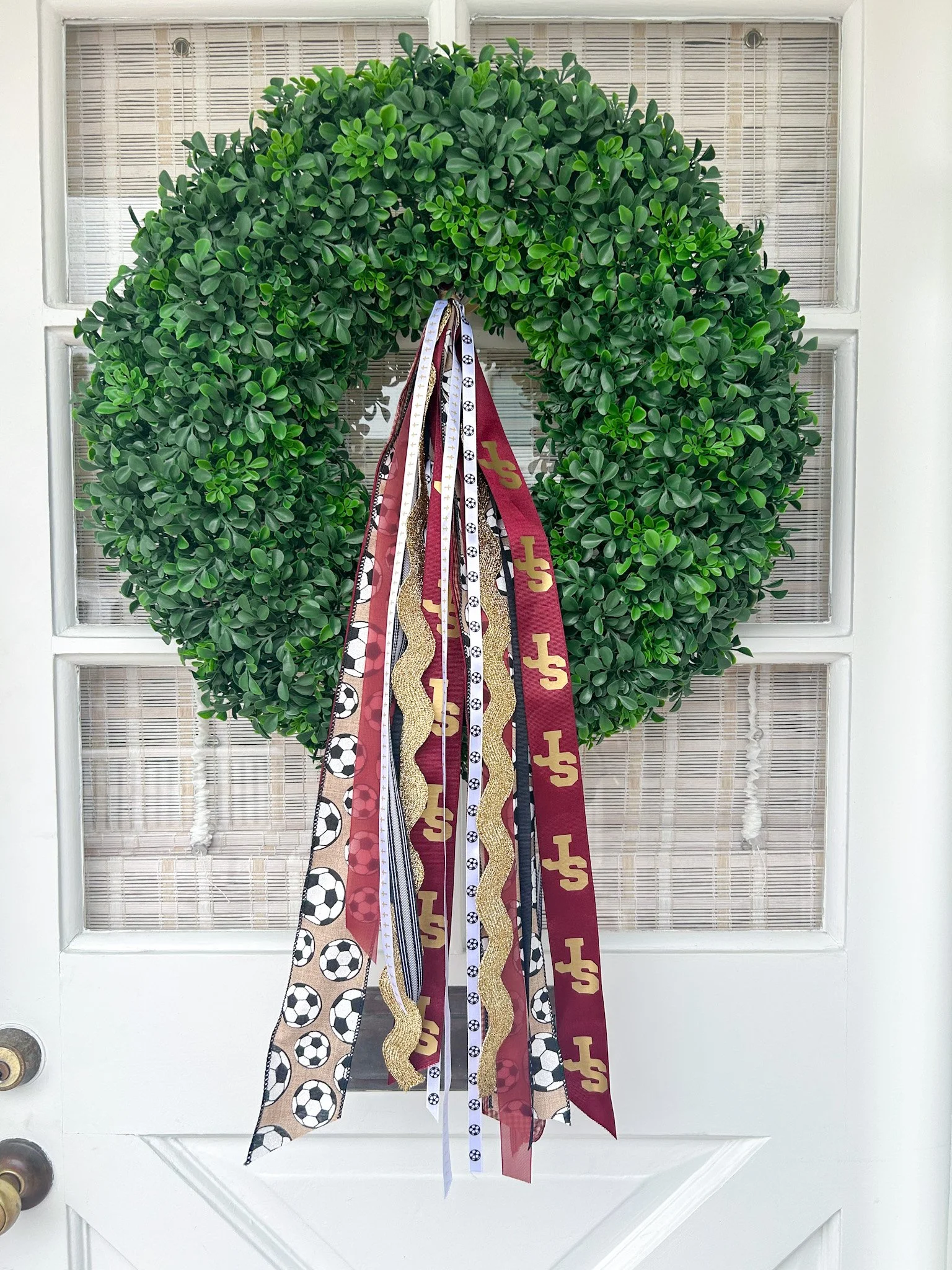 Green wreath with various sports-themed ribbons hanging in the center, decorating a white door.
