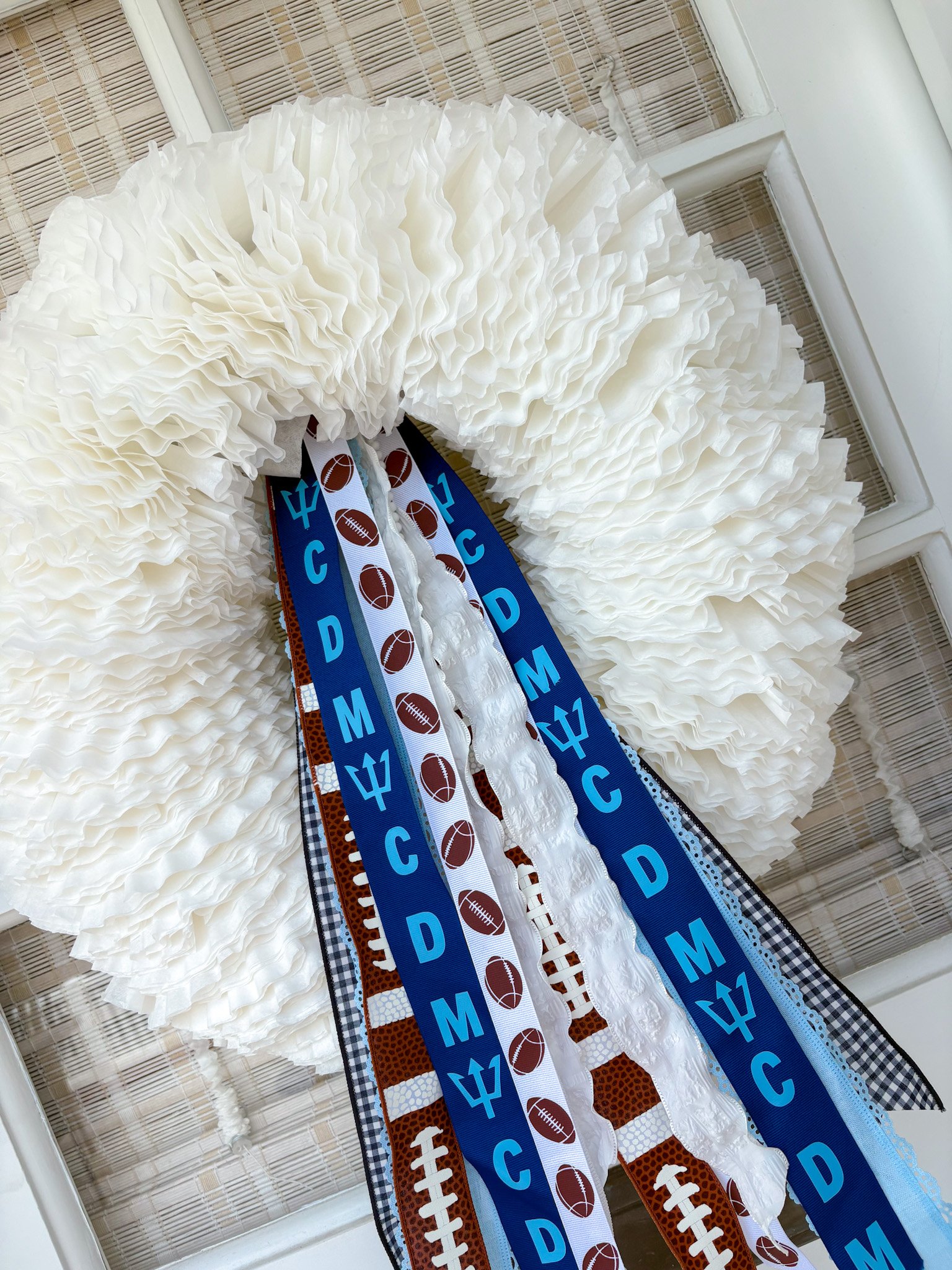 A white football wreath decorated with ribbons featuring football patterns and corona Del Mar high, hanging on a front door.