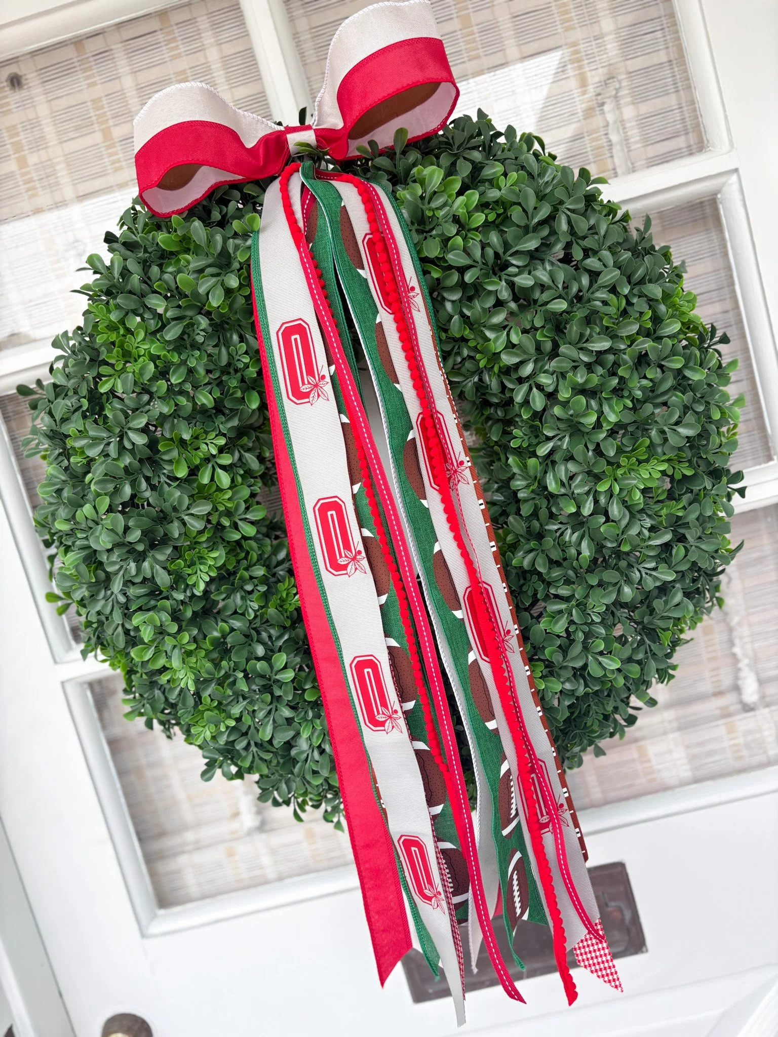 A decorative sports wreath version with red, white, green, and patterned ribbons hanging from the top, mounted on a door with a window.