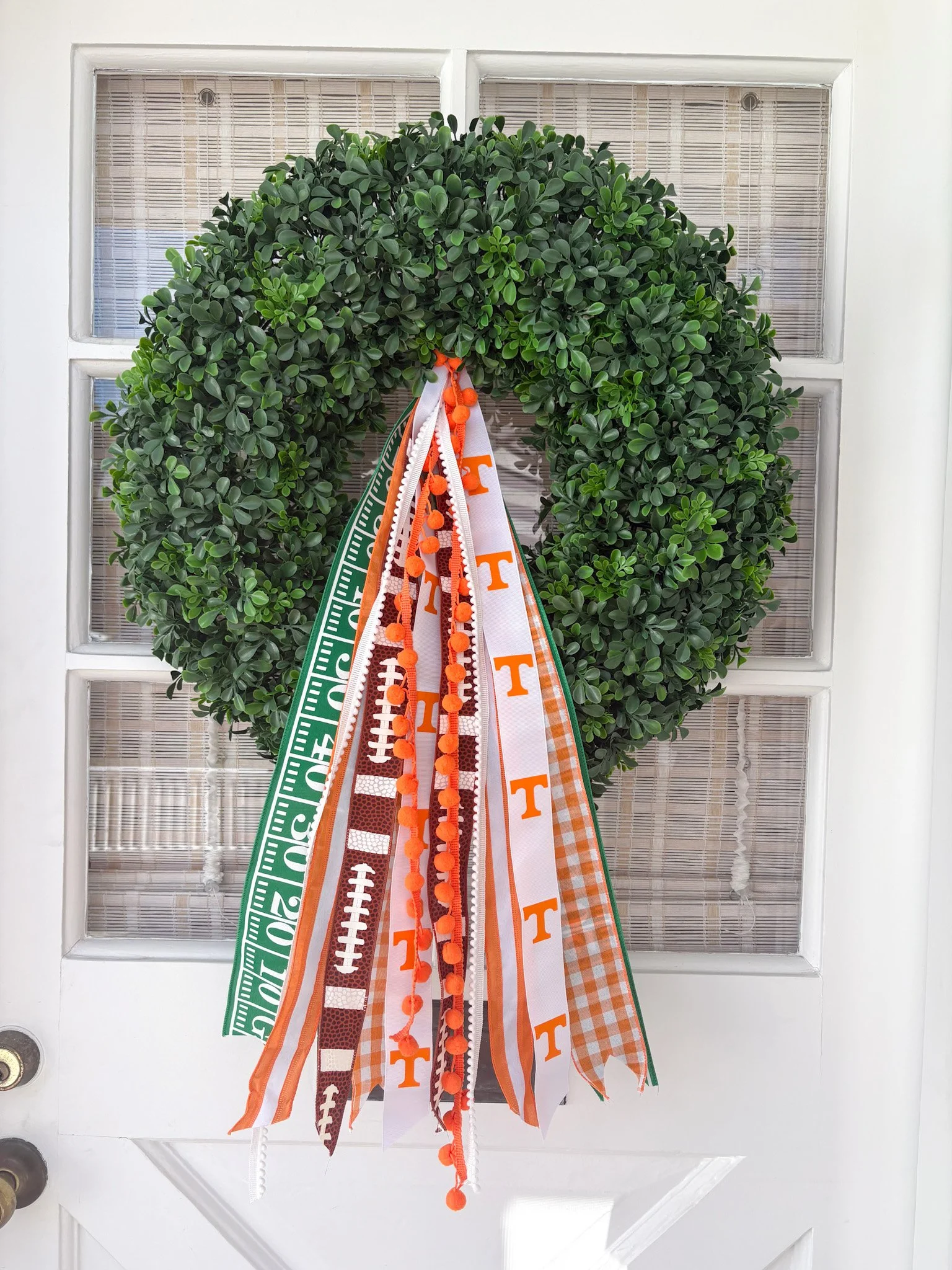 Green wreath with university-themed ribbons and orange pom-pom trim hanging on a white door.