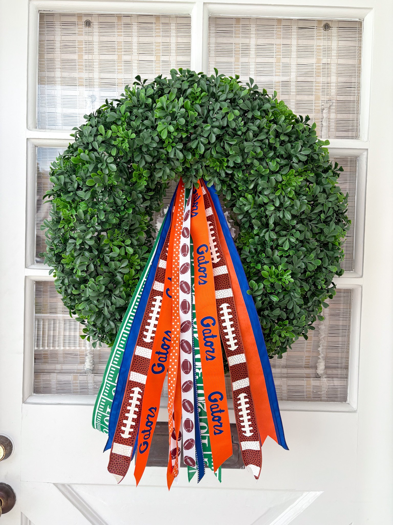 A decorative wreath made of greenery with colorful ribbons hanging in front of a glass-paneled door.