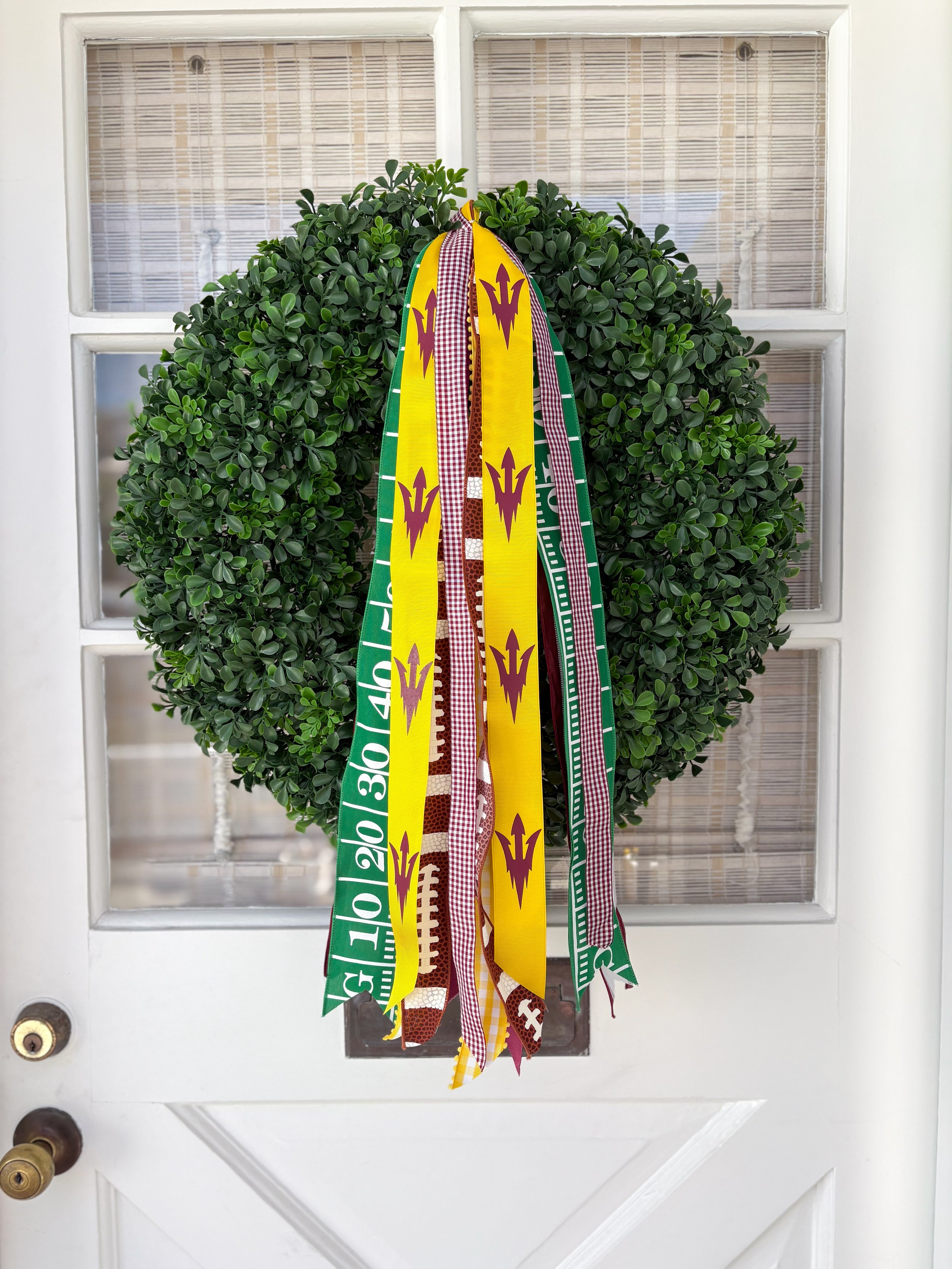 A decorative sports wreath, adorned with colorful ribbons in yellow,  white, and red patterns for sun devils.