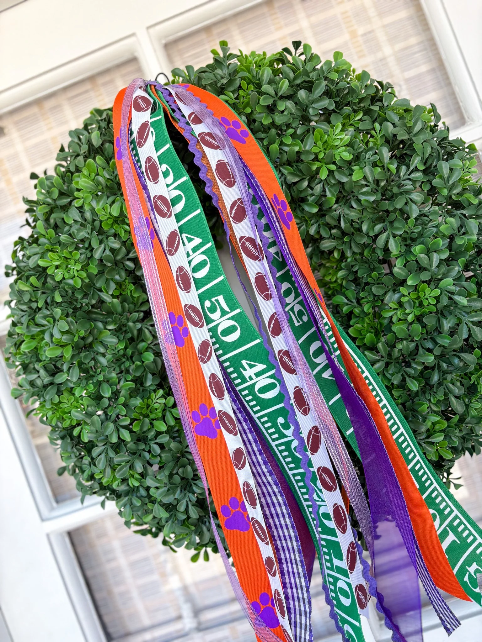 Colorful rally ribbons with football and paw print patterns hanging on a green boxwood wreath.
