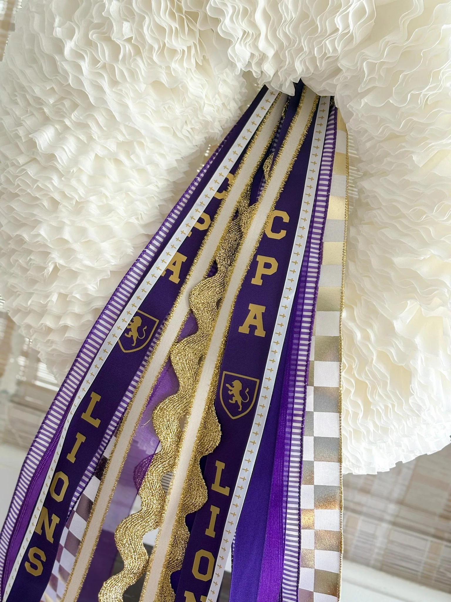 Close-up of a wreath decorated with purple and gold ribbons, featuring the letters CPA, and sports themed ribbons.
