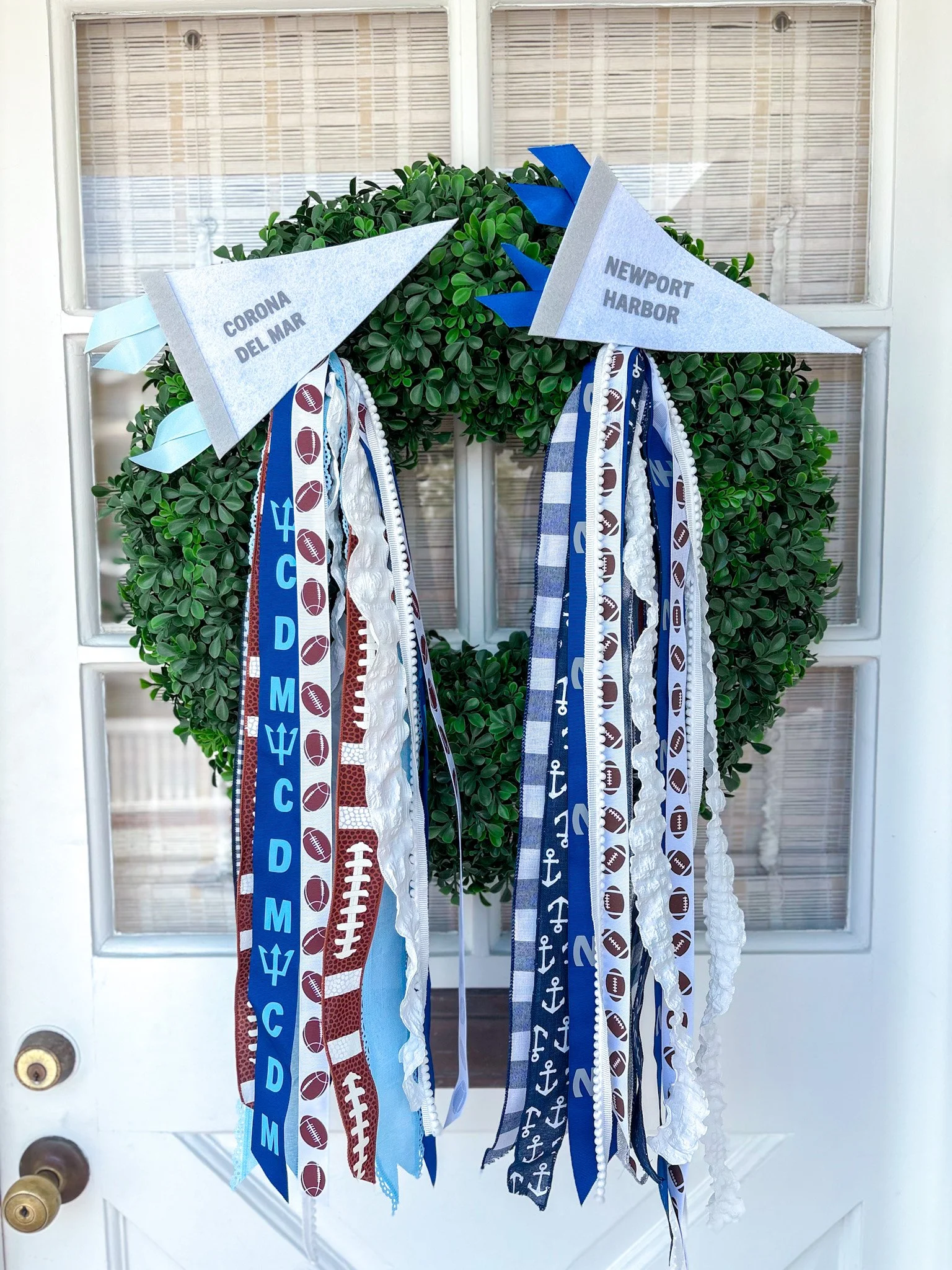 Green door wreath decorated with fabric ribbons and small flags labeled 'Corona Del Mar' and 'Newport Harbor' for a football game or event.