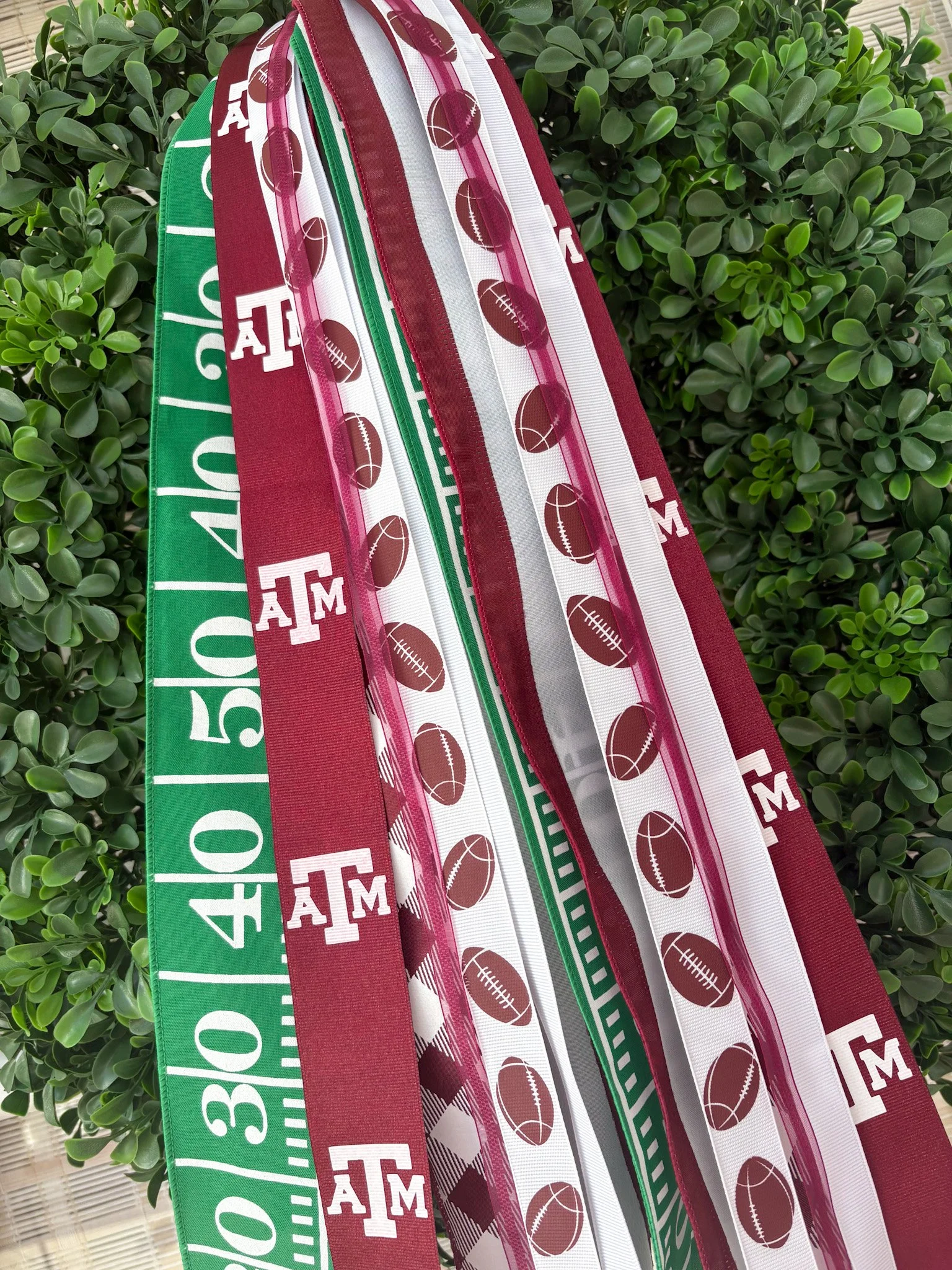 Several colorful rally ribbons with Texas and football-themed designs hanging outdoors against green wreath.