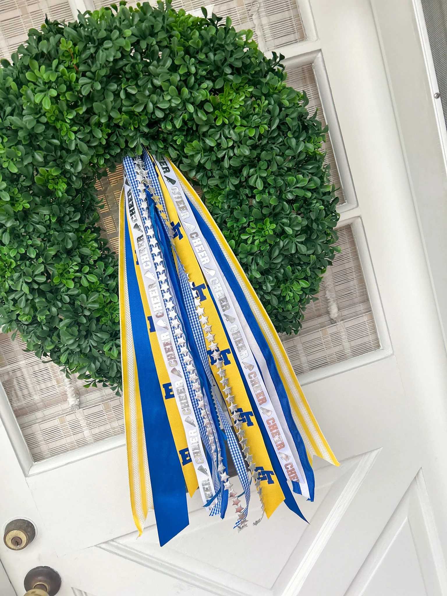 Sports-themed ribbons and banners hanging on a green wreath in front of a white door with glass panels.