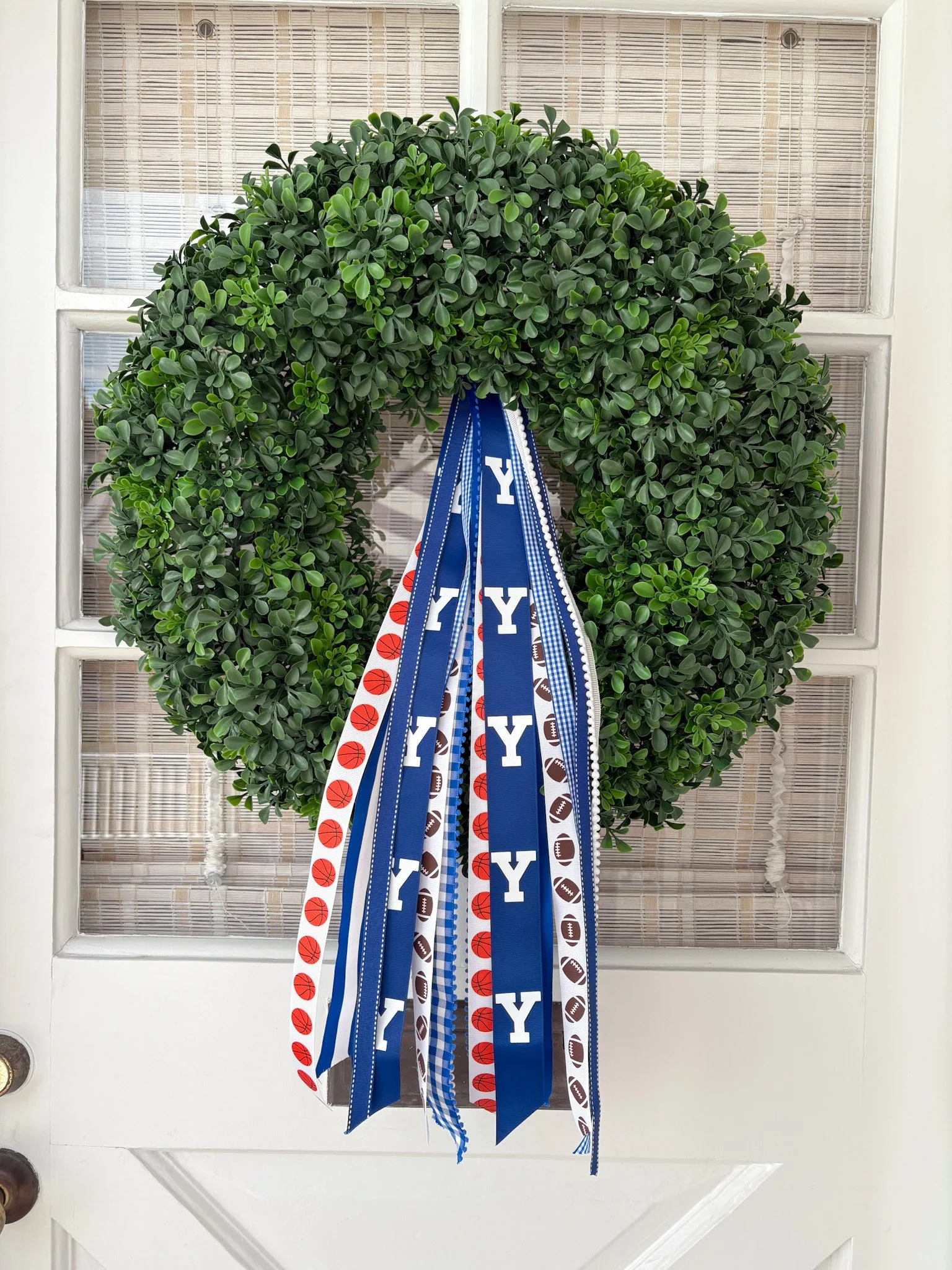 A green wreath decorated with ribbons featuring sports themes and the letter 'Y' hanging on a white door.